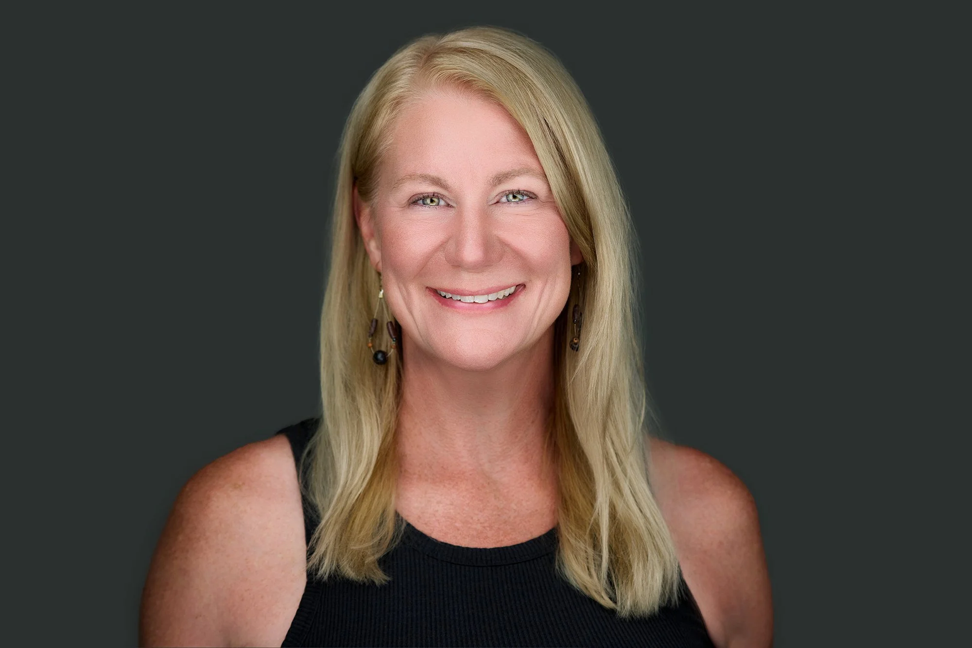 Teresa Petersen, a woman with long blonde hair, blue eyes, and earrings, smiling against a dark background.