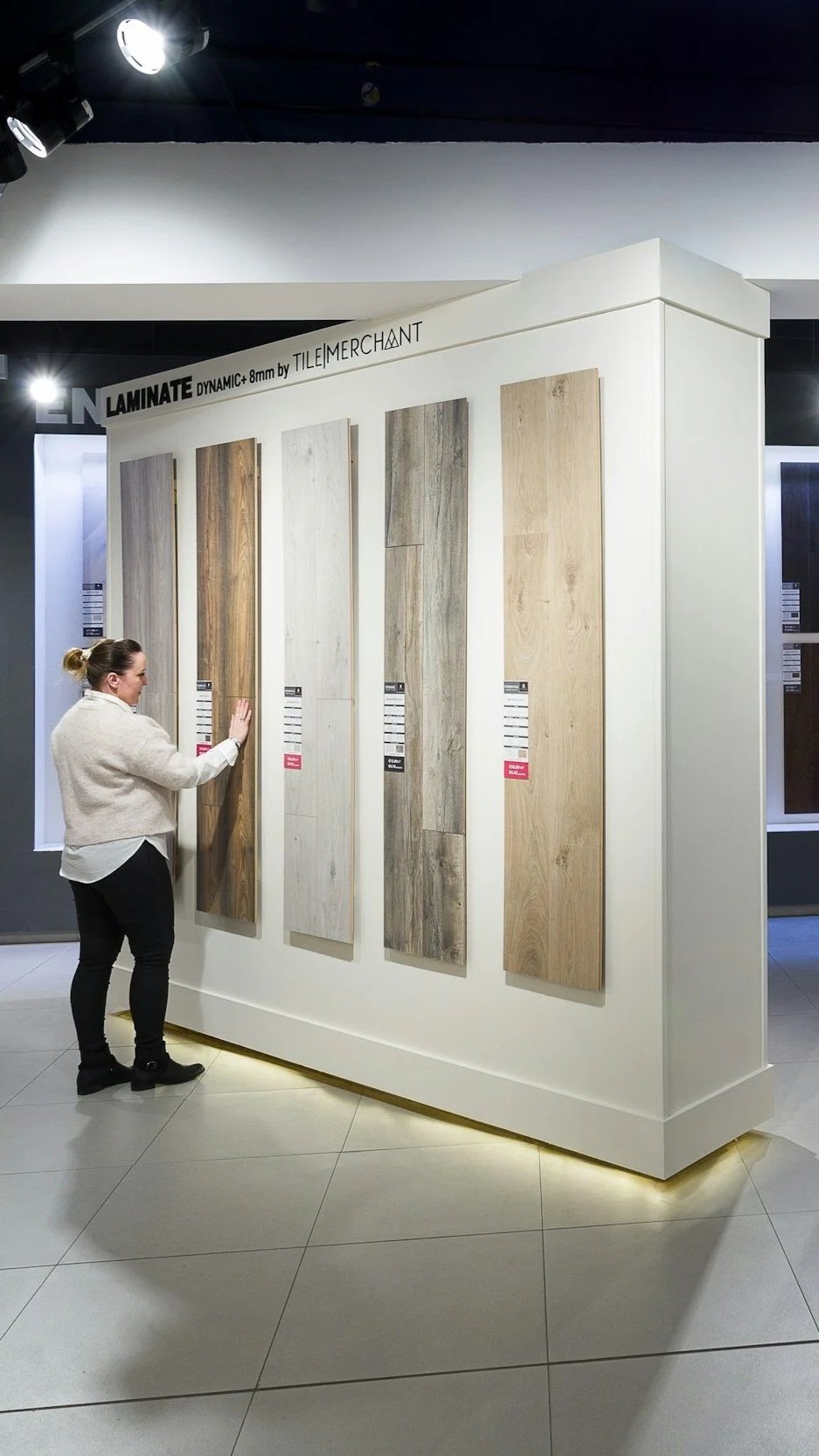 A woman browsing wood laminate samples displayed on a white wall at a store.