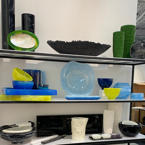 Display of colorful glass and ceramic bowls and vases on glass shelves in a modern interior.