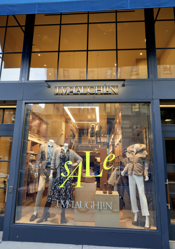 Storefront for J. McLaughlin with mannequins dressed in women's clothing inside, sale sign on window.