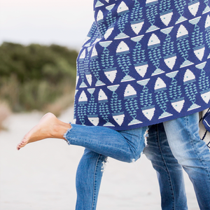 Person carrying a child on their back at the beach, with sand and greenery in the background.