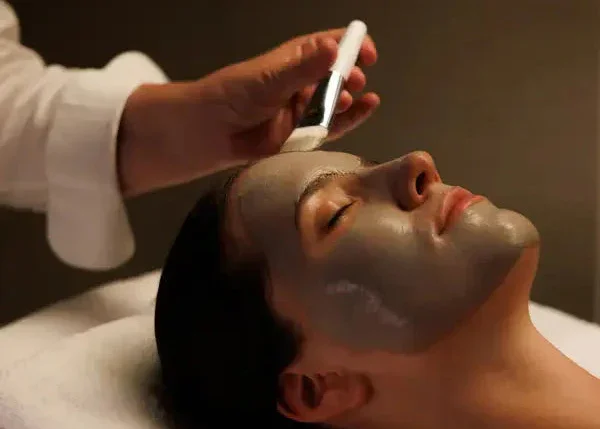 A woman receiving a facial treatment with a mask applied, while a person holds a tool above her face.