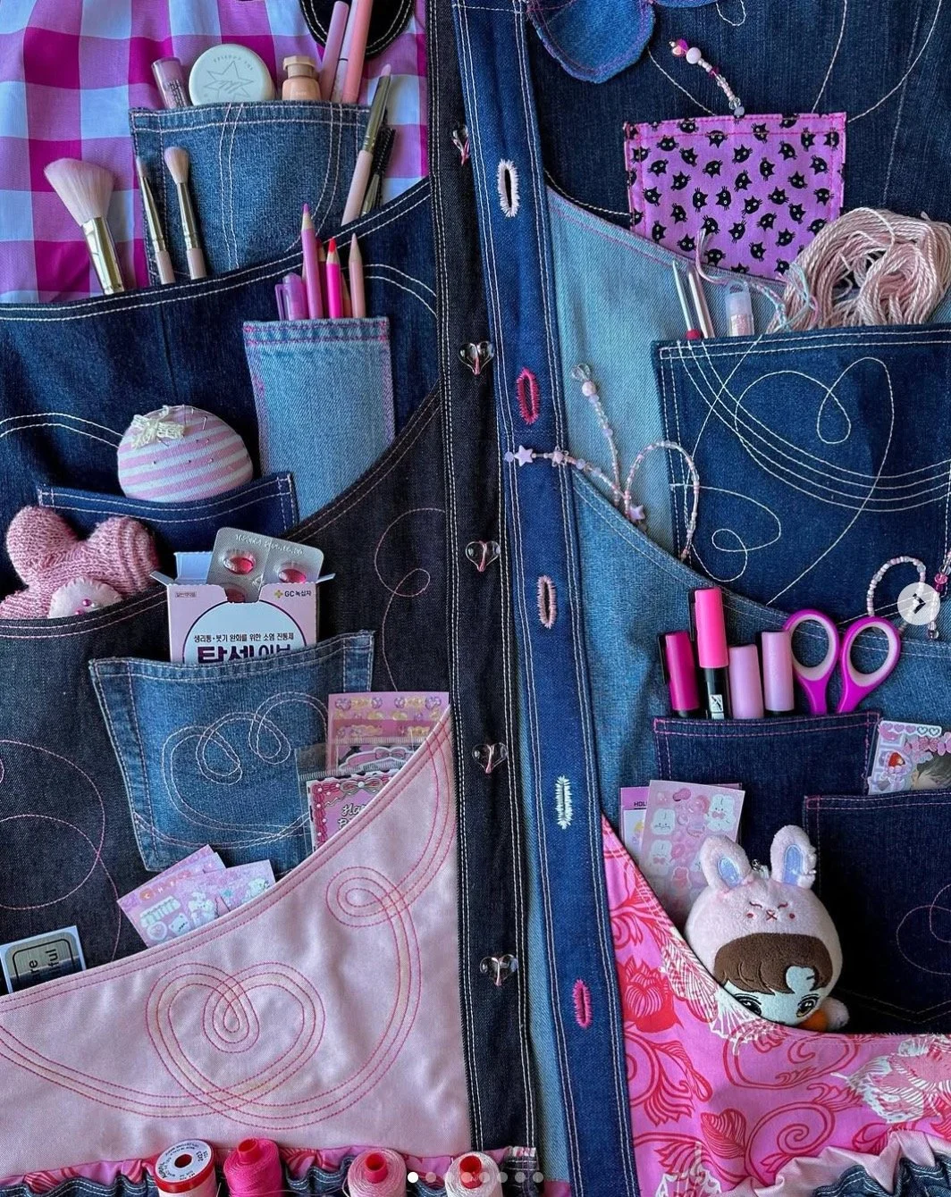 A denim organizer with multiple pink-themed craft supplies, tools, and accessories arranged in pockets and compartments.