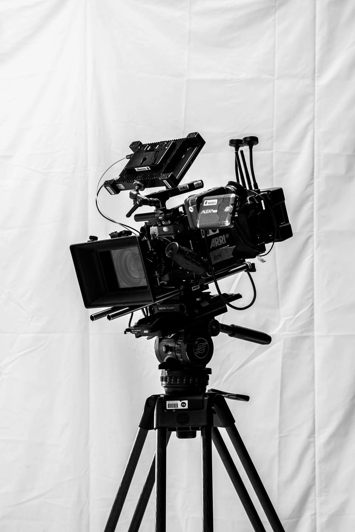 Black professional video camera mounted on tripod with a plain white backdrop