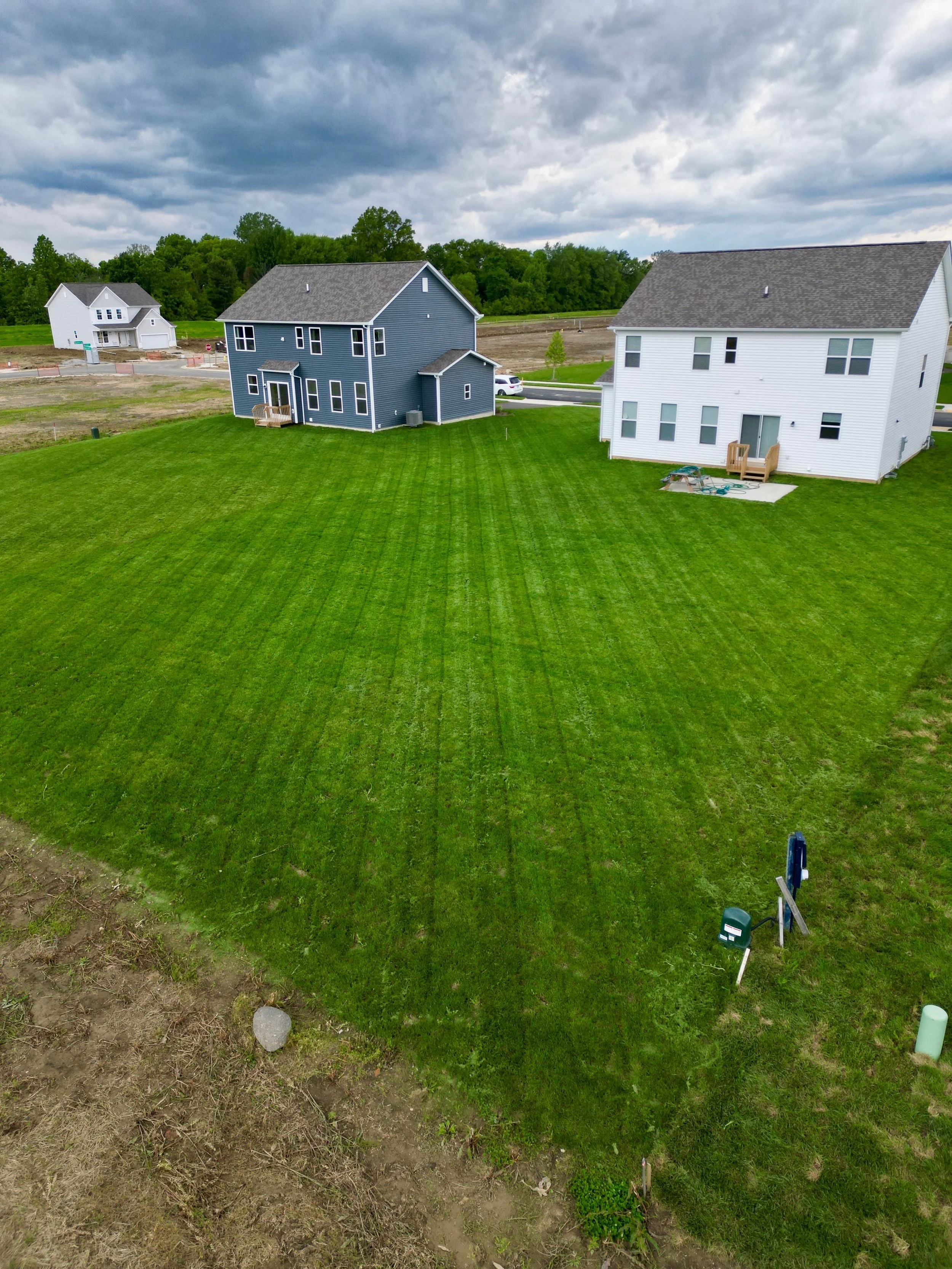 Aerial view of two newly built houses with green lawns in a residential area, under a cloudy sky.