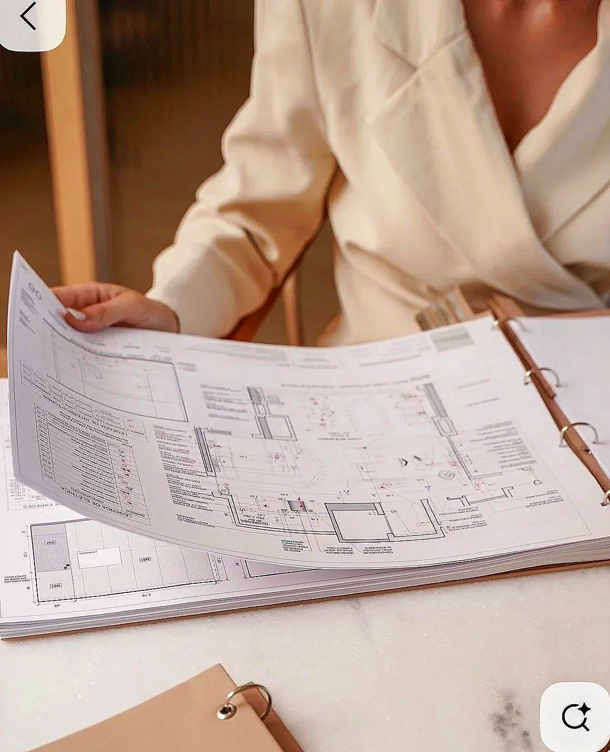 Person in a white shirt holding a large printed architectural blueprint or floor plan over a table.