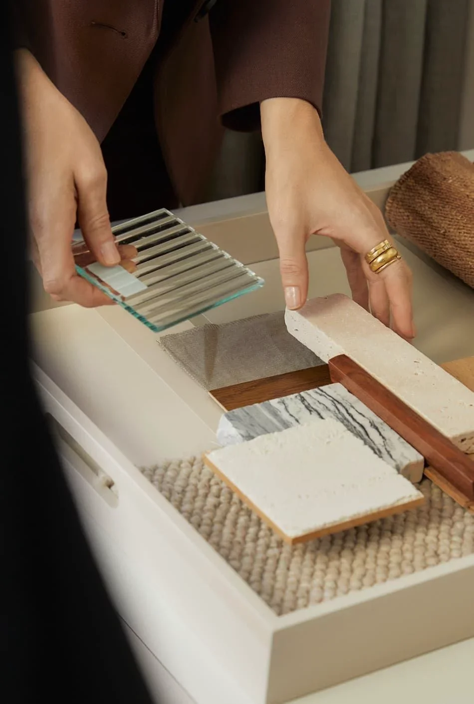 Person arranging various stone, tile, and wood samples on a table.