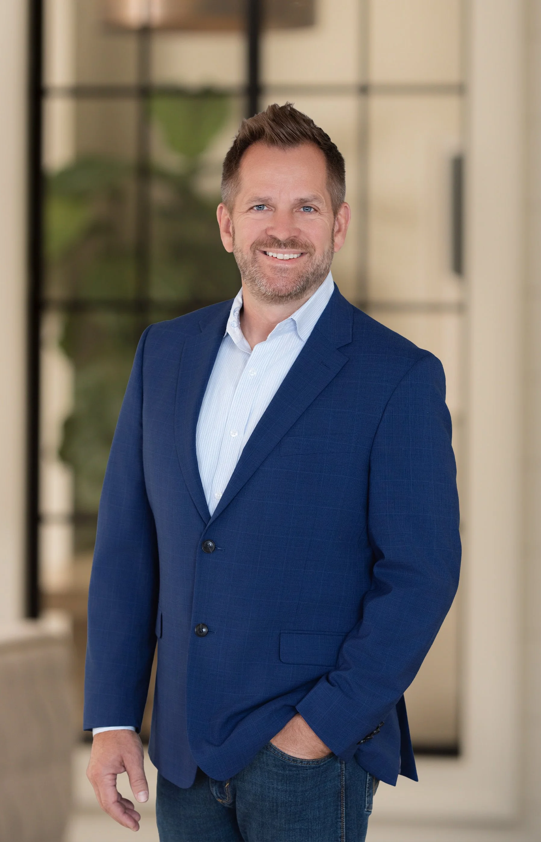 Smiling man in a blue blazer and white shirt posing indoors.
