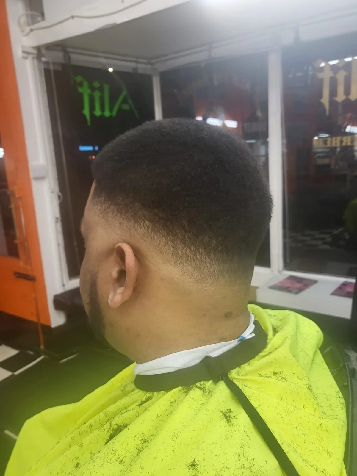 Man in a yellow barber cape sitting in a barber shop with freshly cut fade hairstyle, looking away from the camera.
