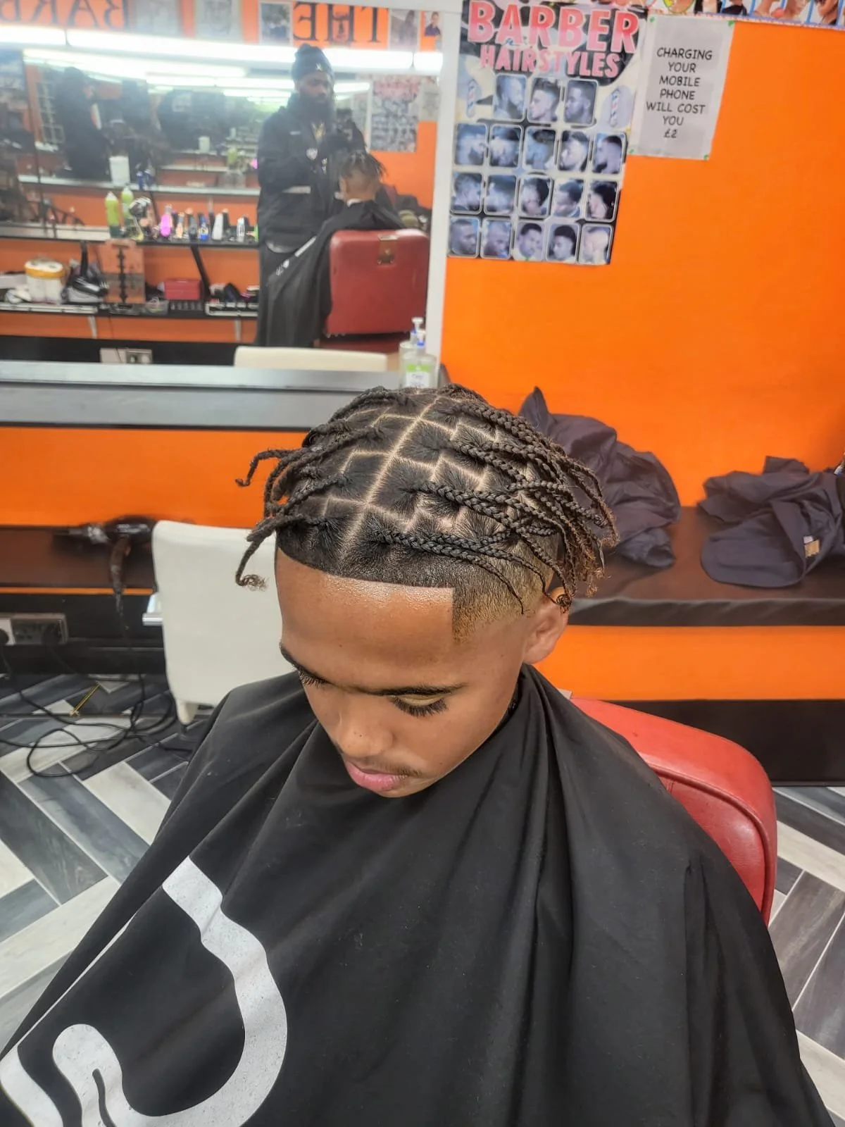 A young man with new braids gets his hair styled at a barbershop.