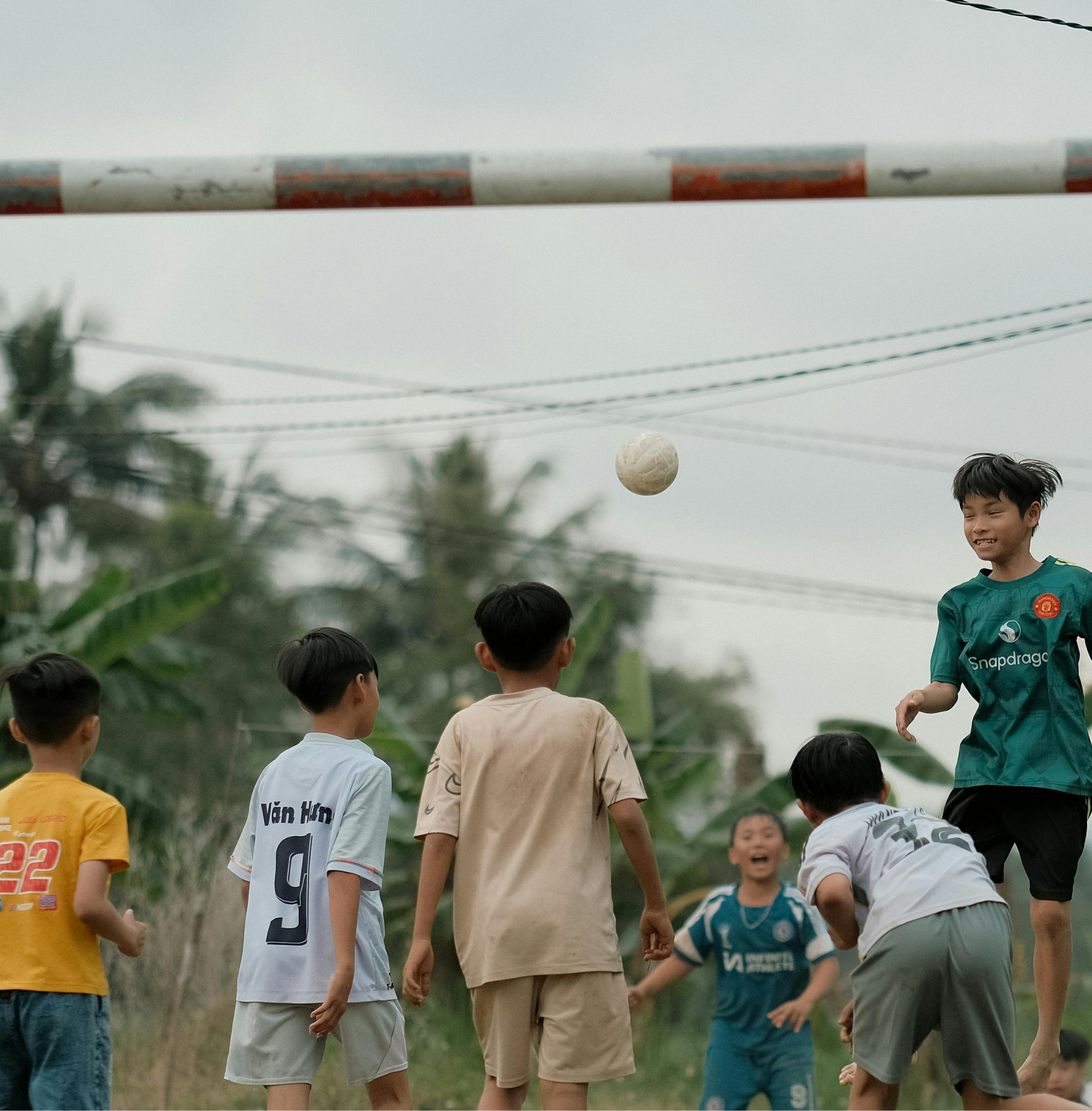 A group of children playing soccer outdoors on a grassy field, watching the ball in midair as one child jumps to head it.