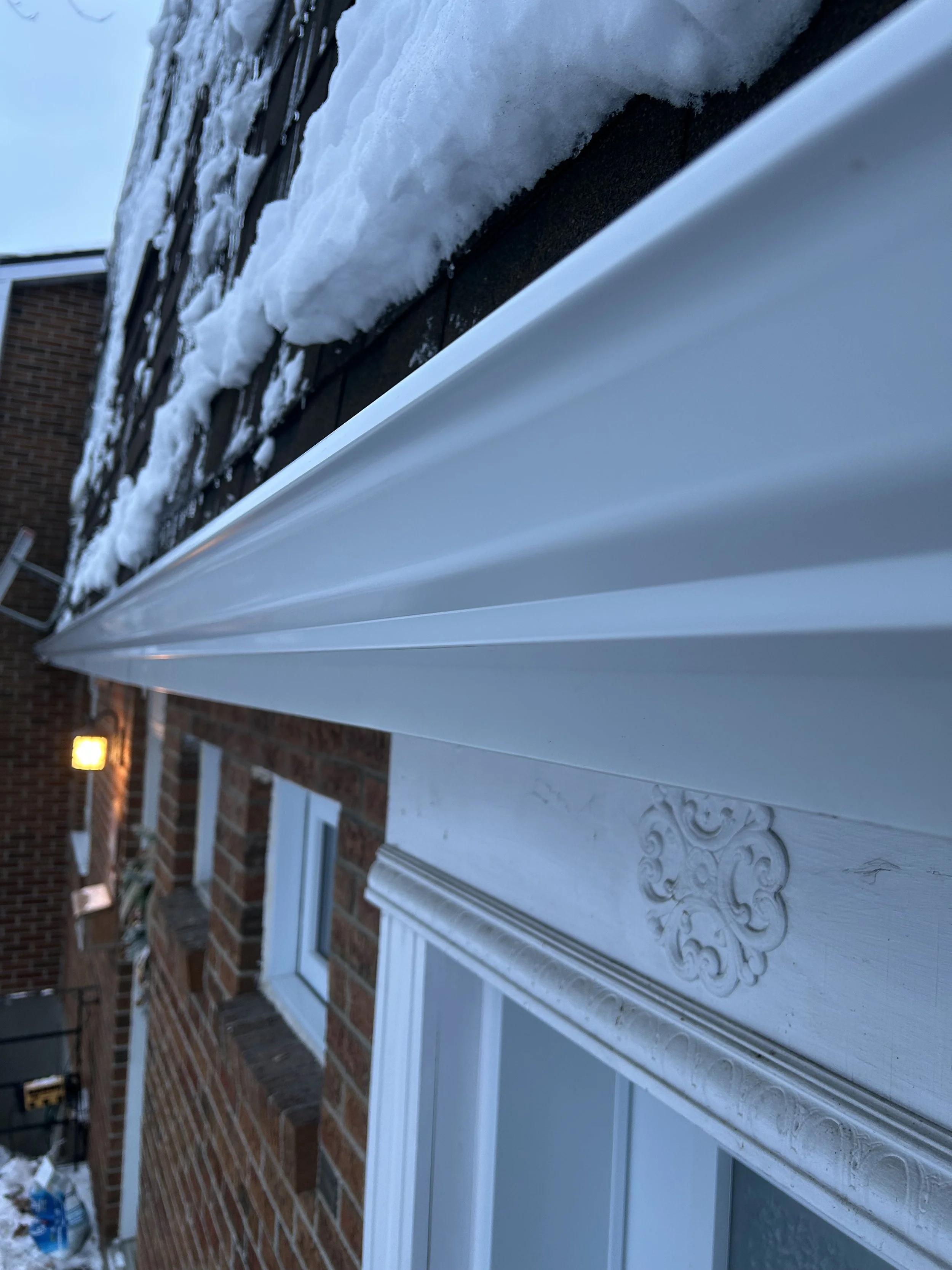 Photo de la façade d'une maison avec un auvent blanc en métal et une brique rouge. Il y a de la neige sur le toit en ardoise.