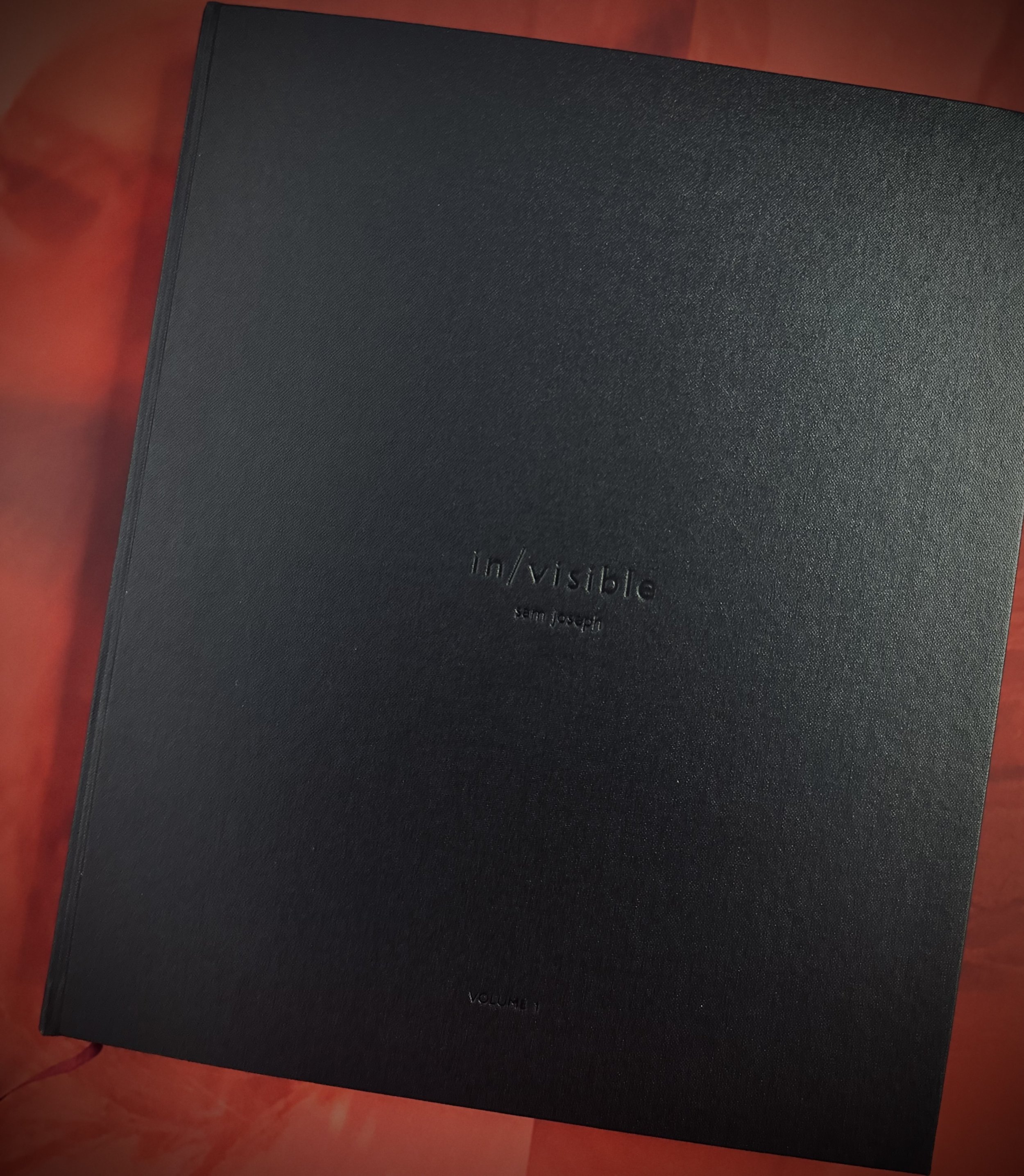 Close-up of a black hardcover book titled "Invisibles" by Sem Joseph, placed on a reddish-brown wooden surface.