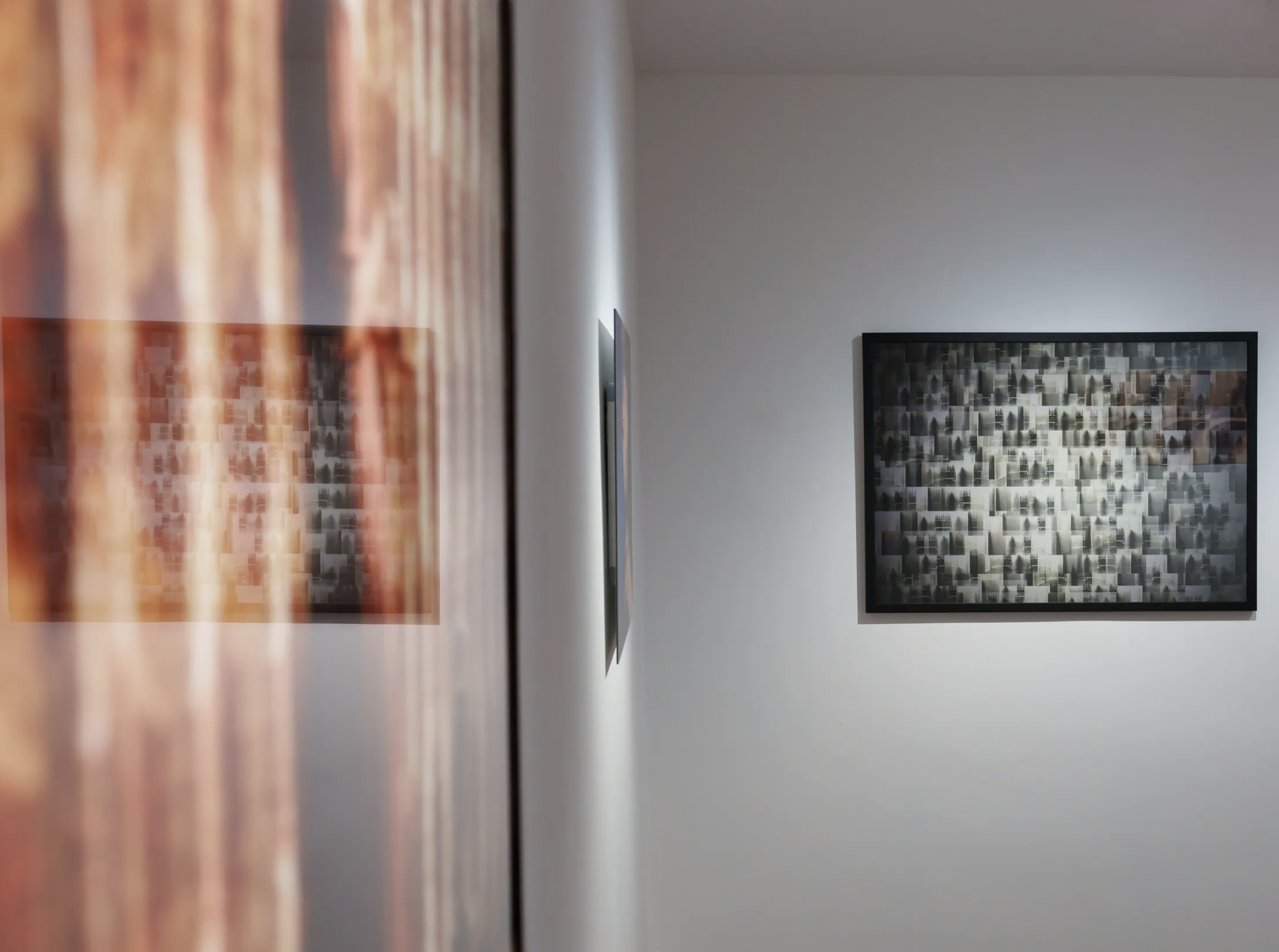 Photo of an art gallery wall displaying two framed abstract paintings, with the photo taken at an angle showing the frames and the textured gallery wall.