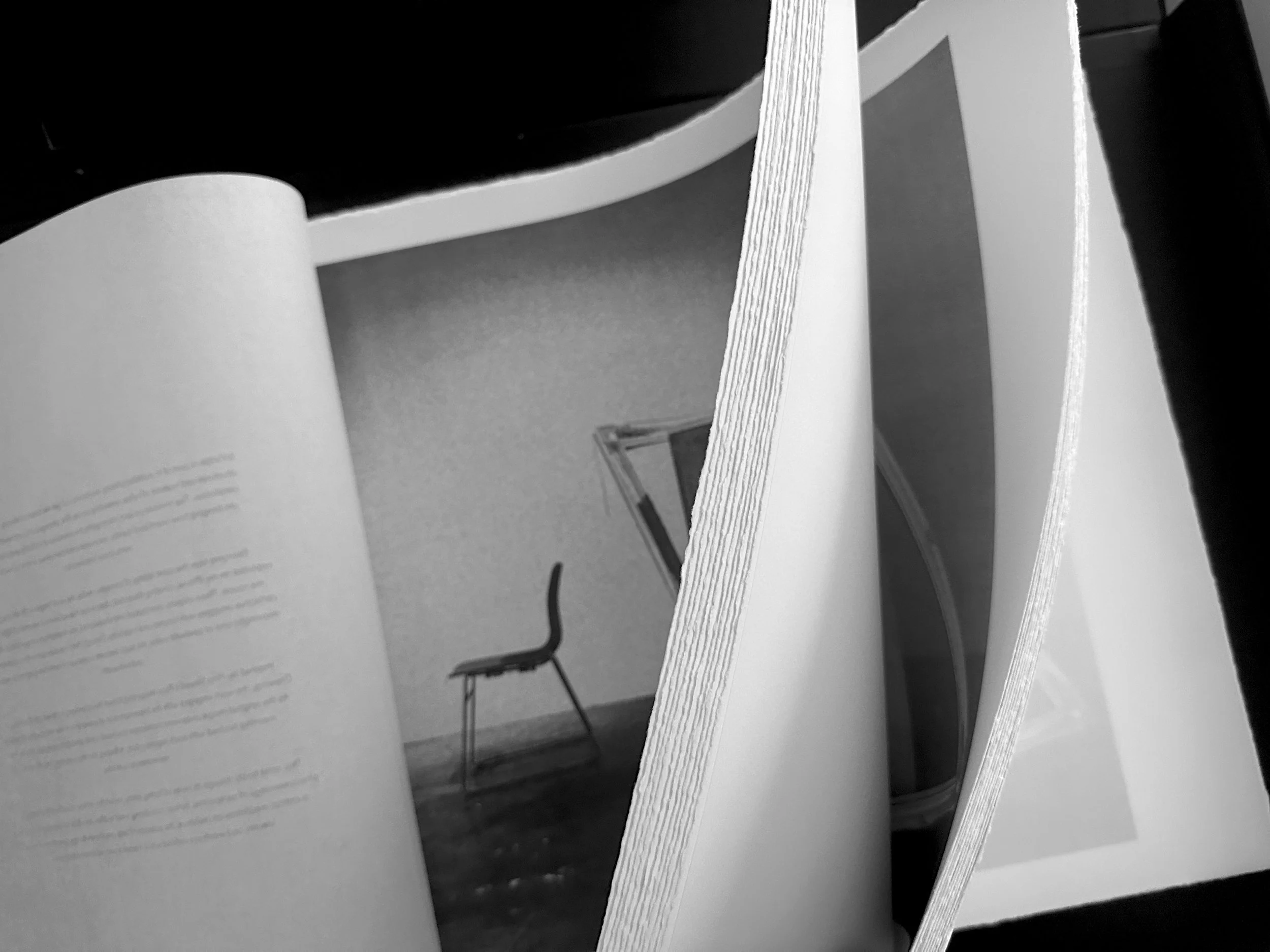 Black and white photo of pages in a book or magazine with a drawing of a chair and part of a bookshelf in the background.