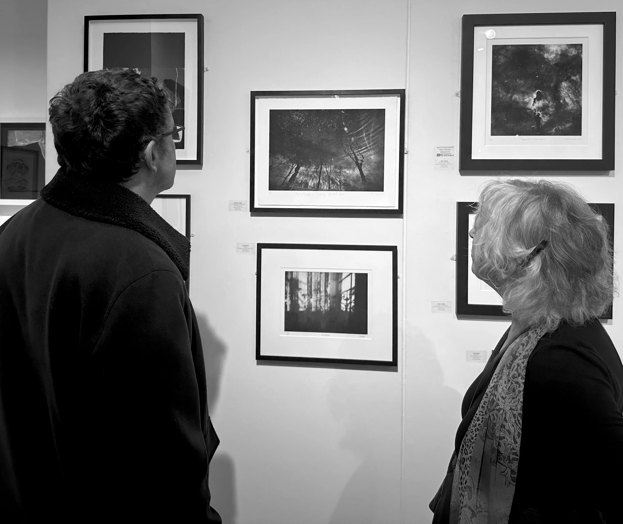 Two women and a man observing framed astrophotography pictures on a gallery wall.