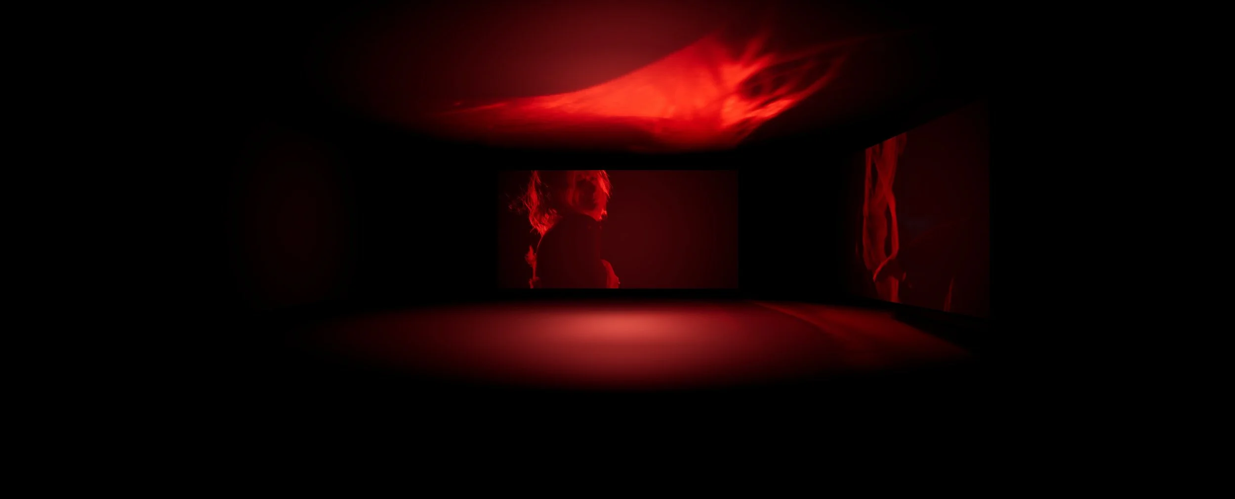 Dark room with multiple screens displaying red-tinted images of a person with curly hair.