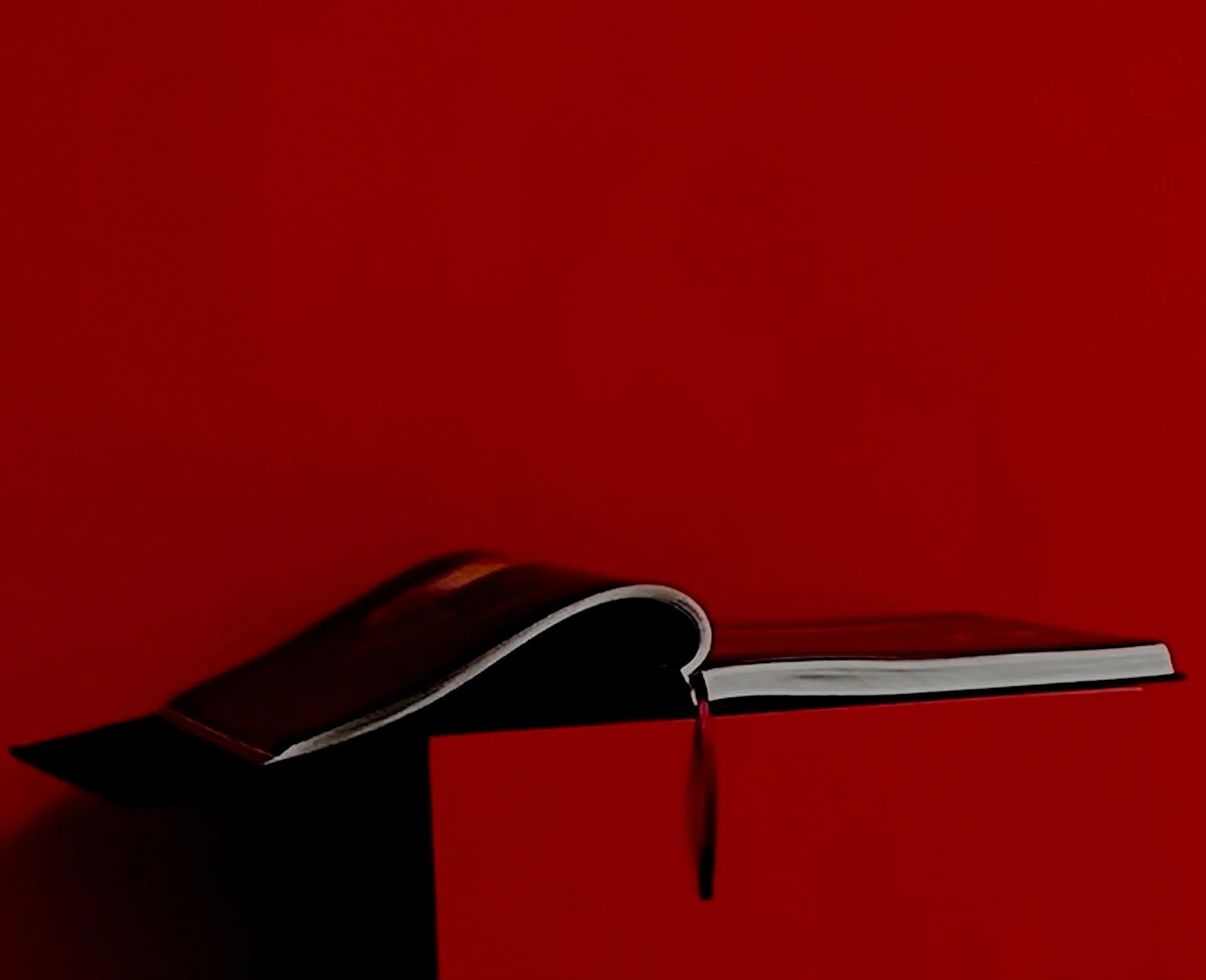 Part of an open book resting on a black stand against a red background.