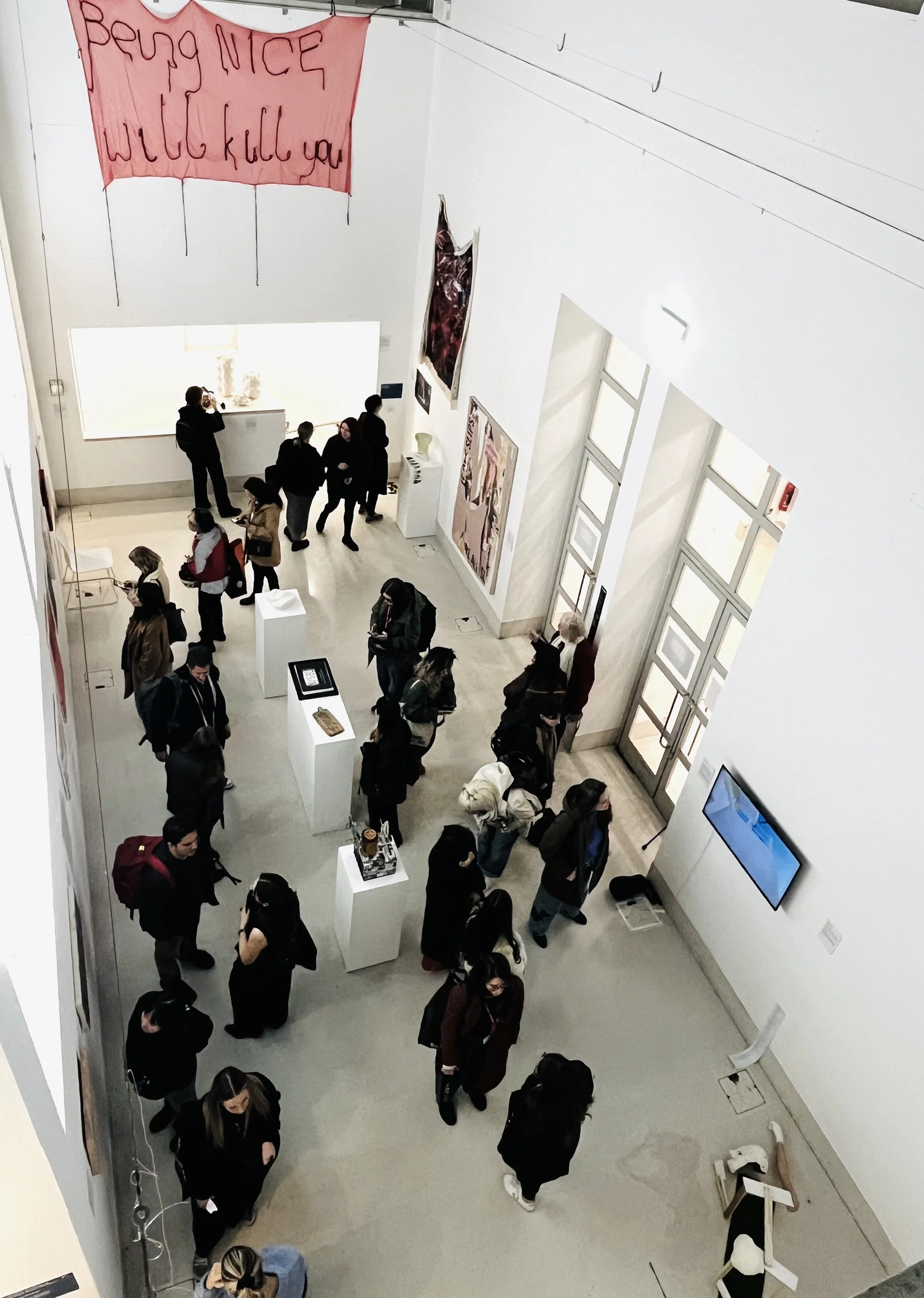 People visiting an art gallery with paintings on the walls and digital screens, some engaging with artwork or taking pictures.