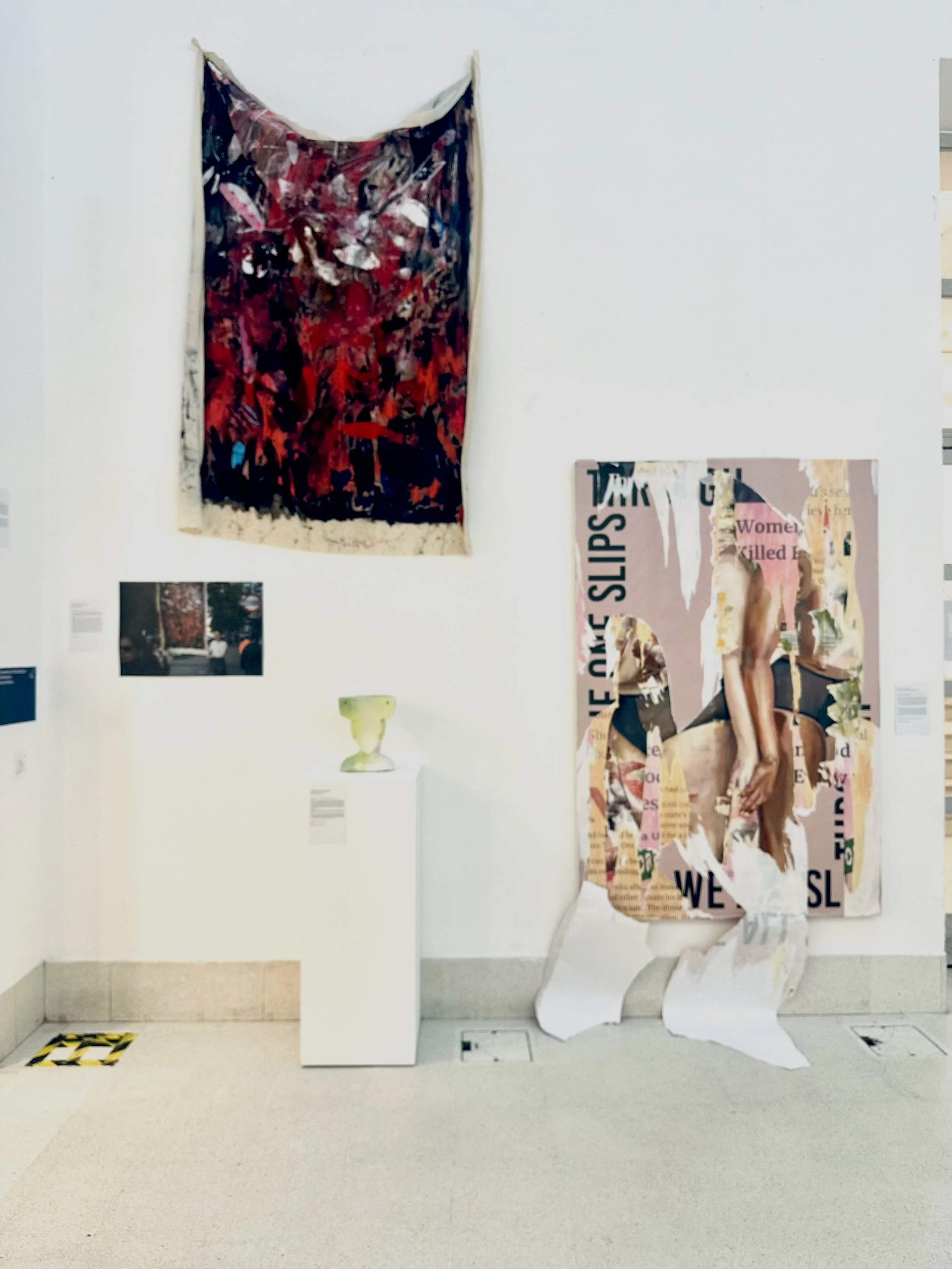 An art gallery with abstract collages and posters on the white wall, a white pedestal, and a white chair.