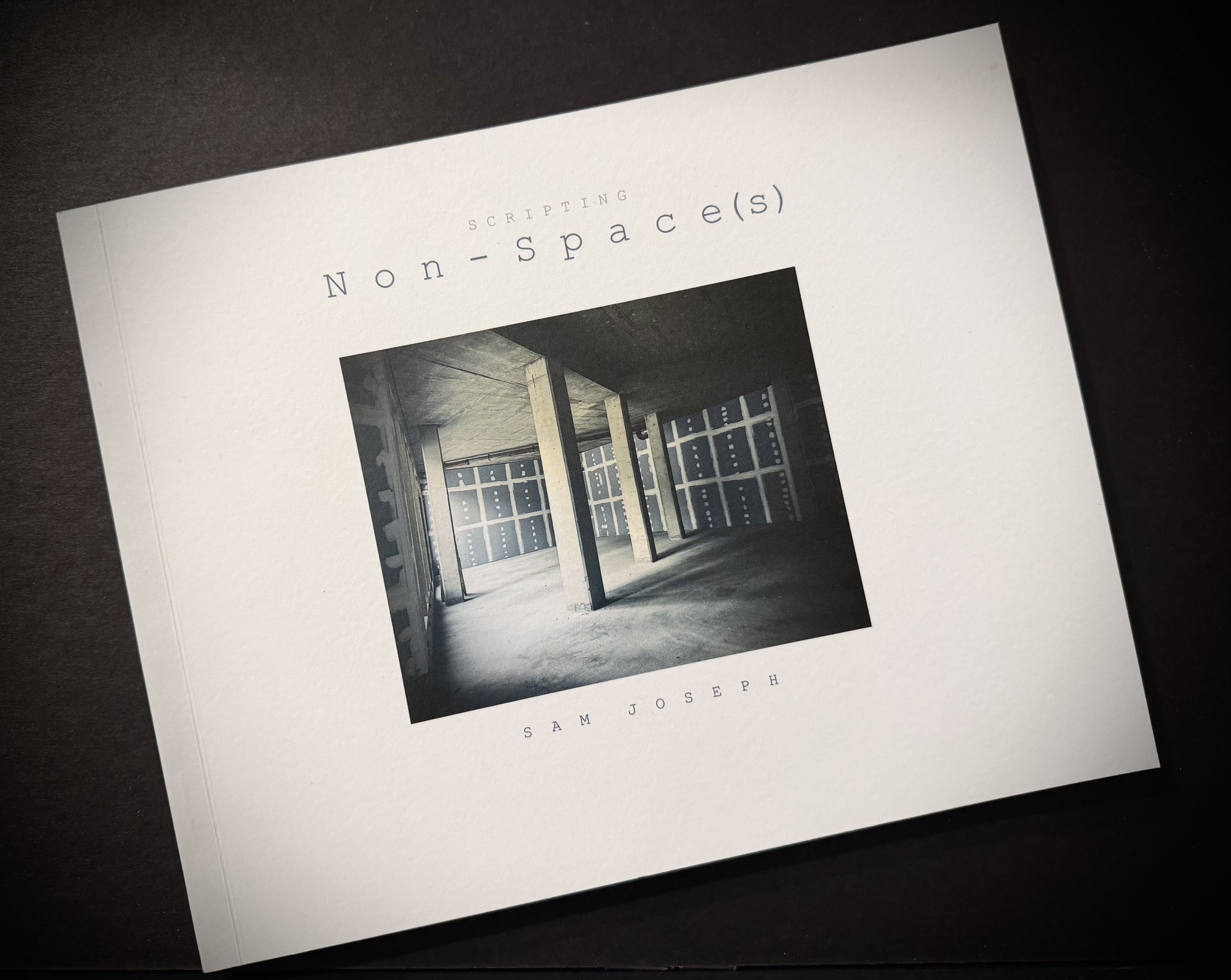 A printed page with the title 'Scripting Non-space(s)' and a black-and-white photograph of an industrial-looking interior space with large windows and structural beams.