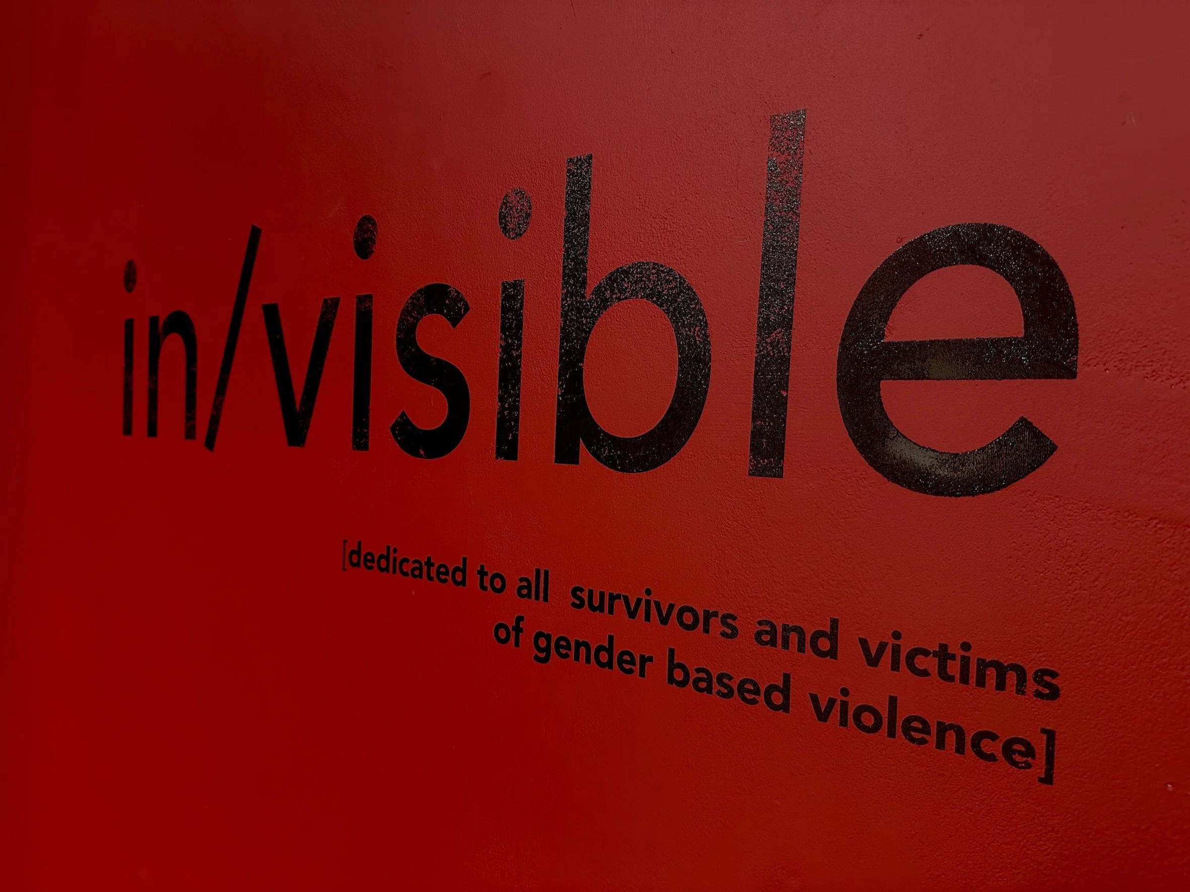 Close-up of a red poster with black text, mentioning survivors and victims of gender-based violence.