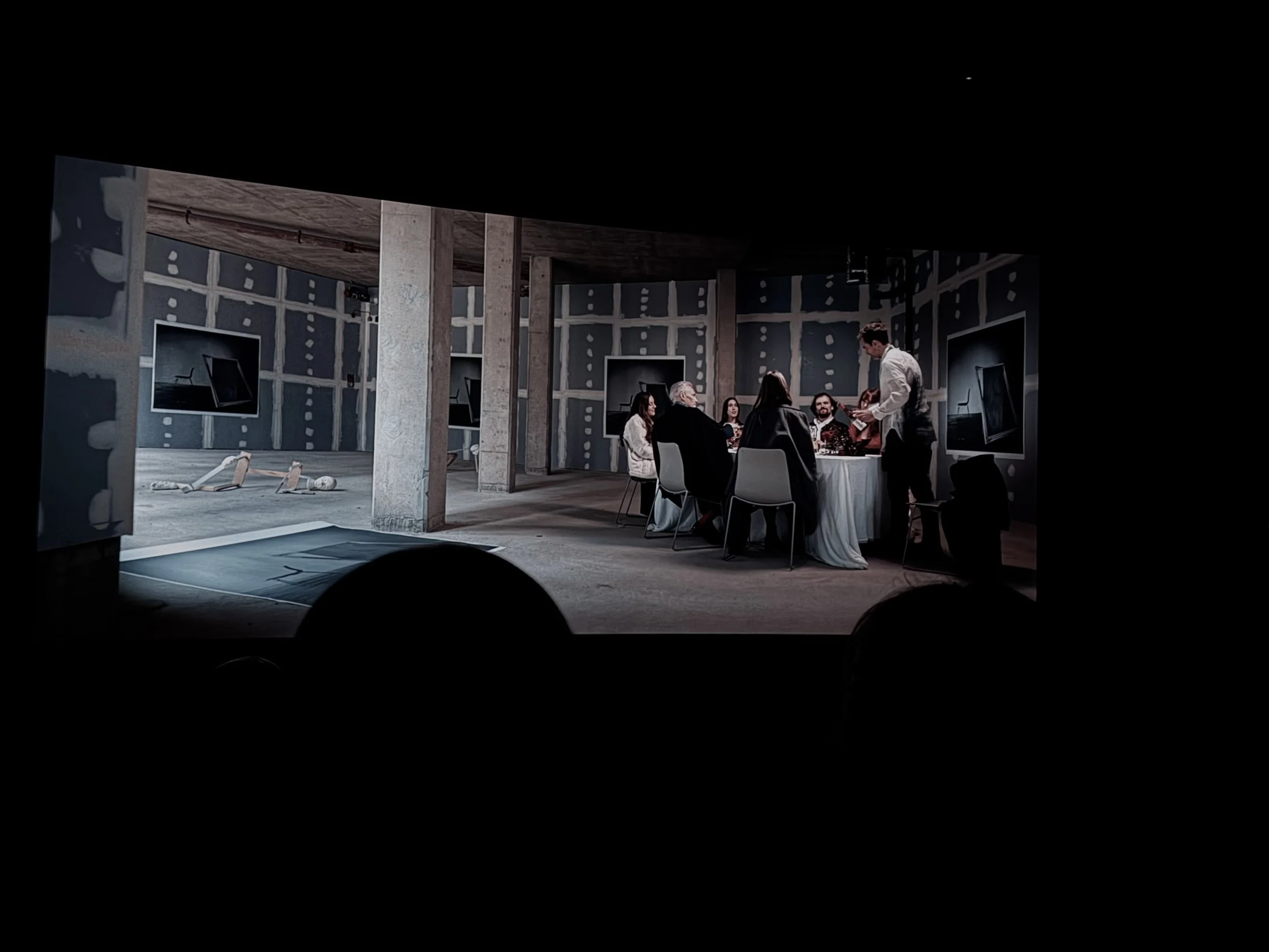 Group of people seated around a table during a meeting or presentation in an industrial-style room with large screens on the wall.