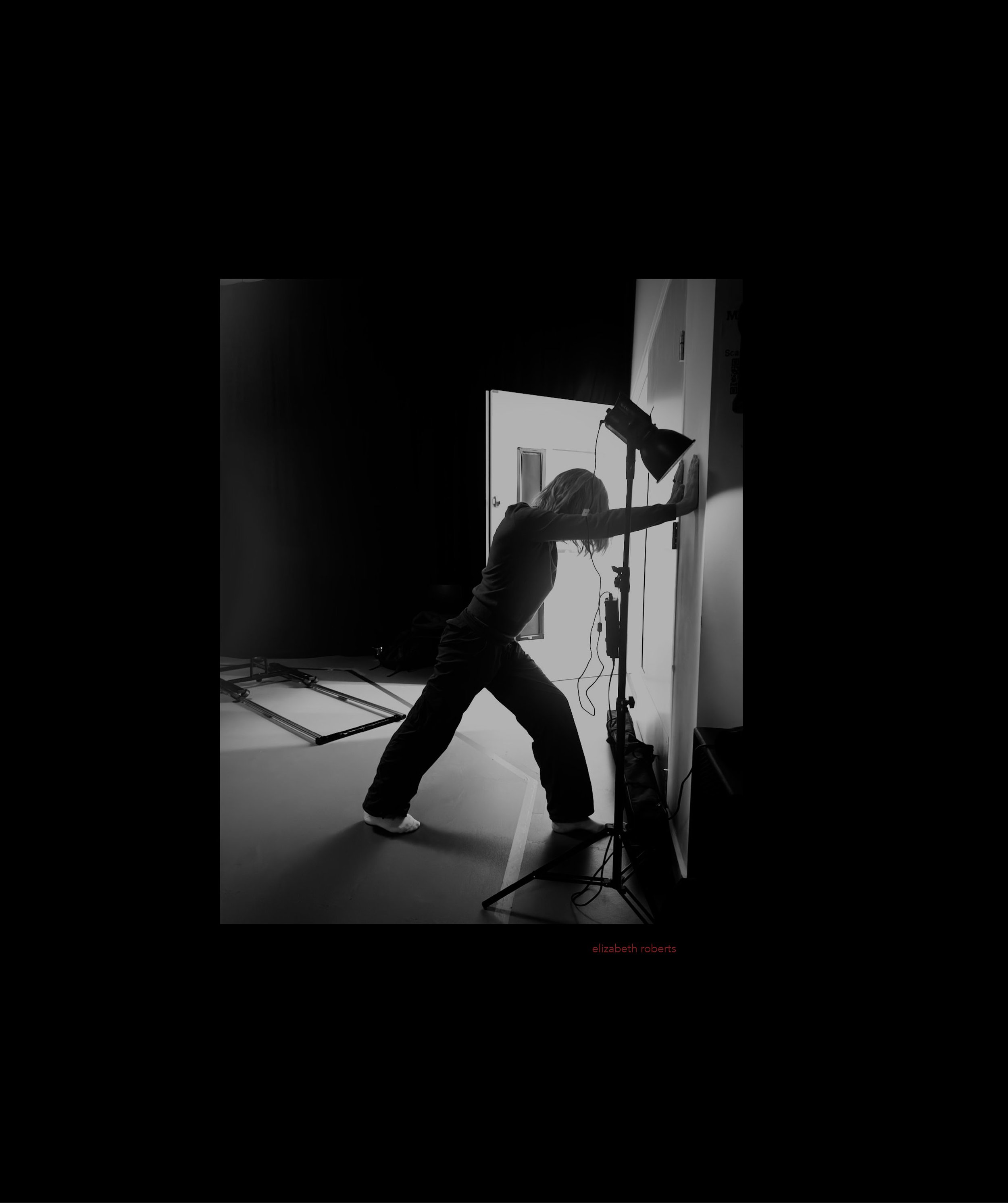 A woman stretching in front of a white screen with studio lighting and equipment in a photography studio.