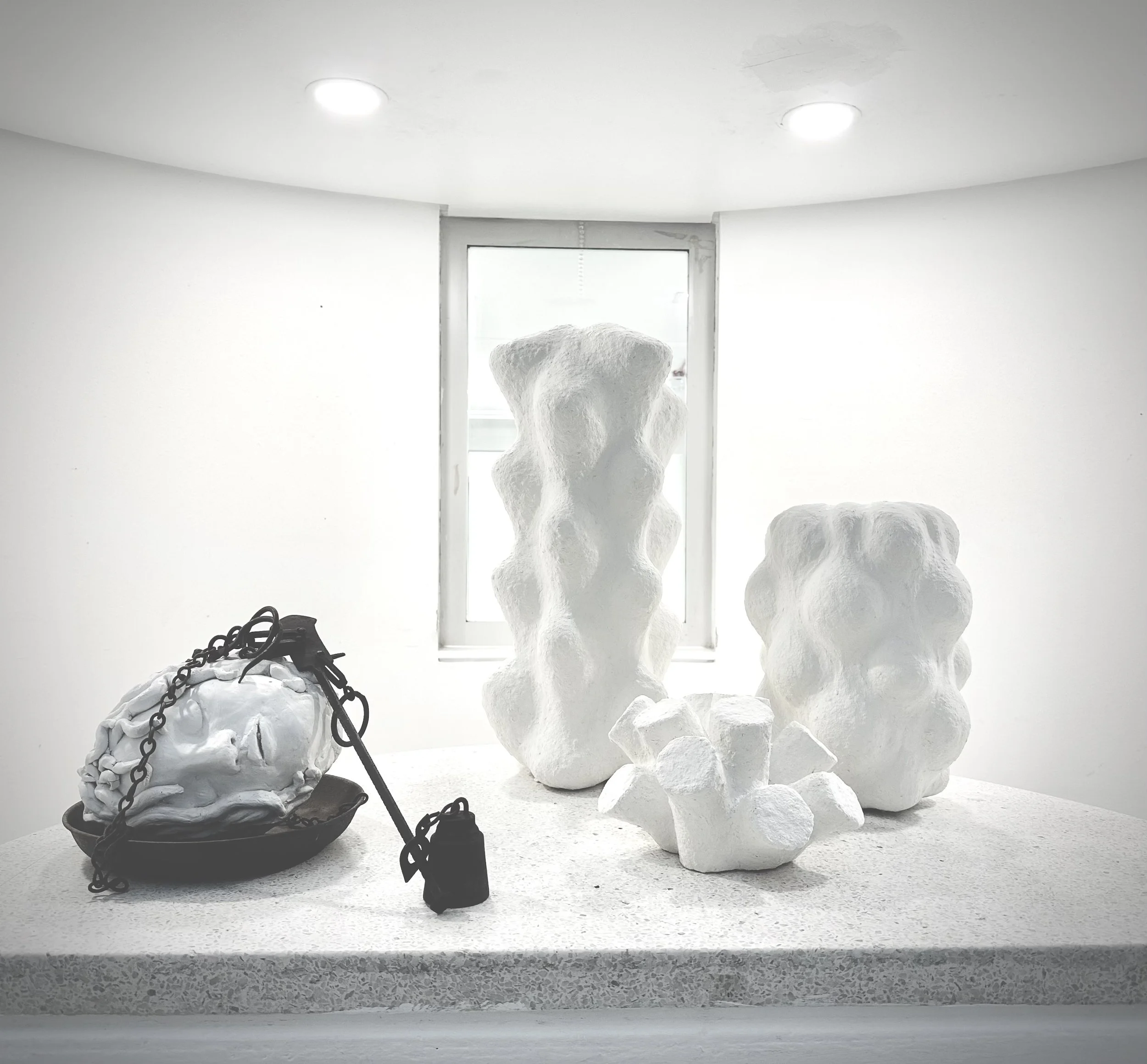 White abstract sculptures resembling organic shapes on a white pedestal in a minimalistic gallery space with bright ceiling lighting.