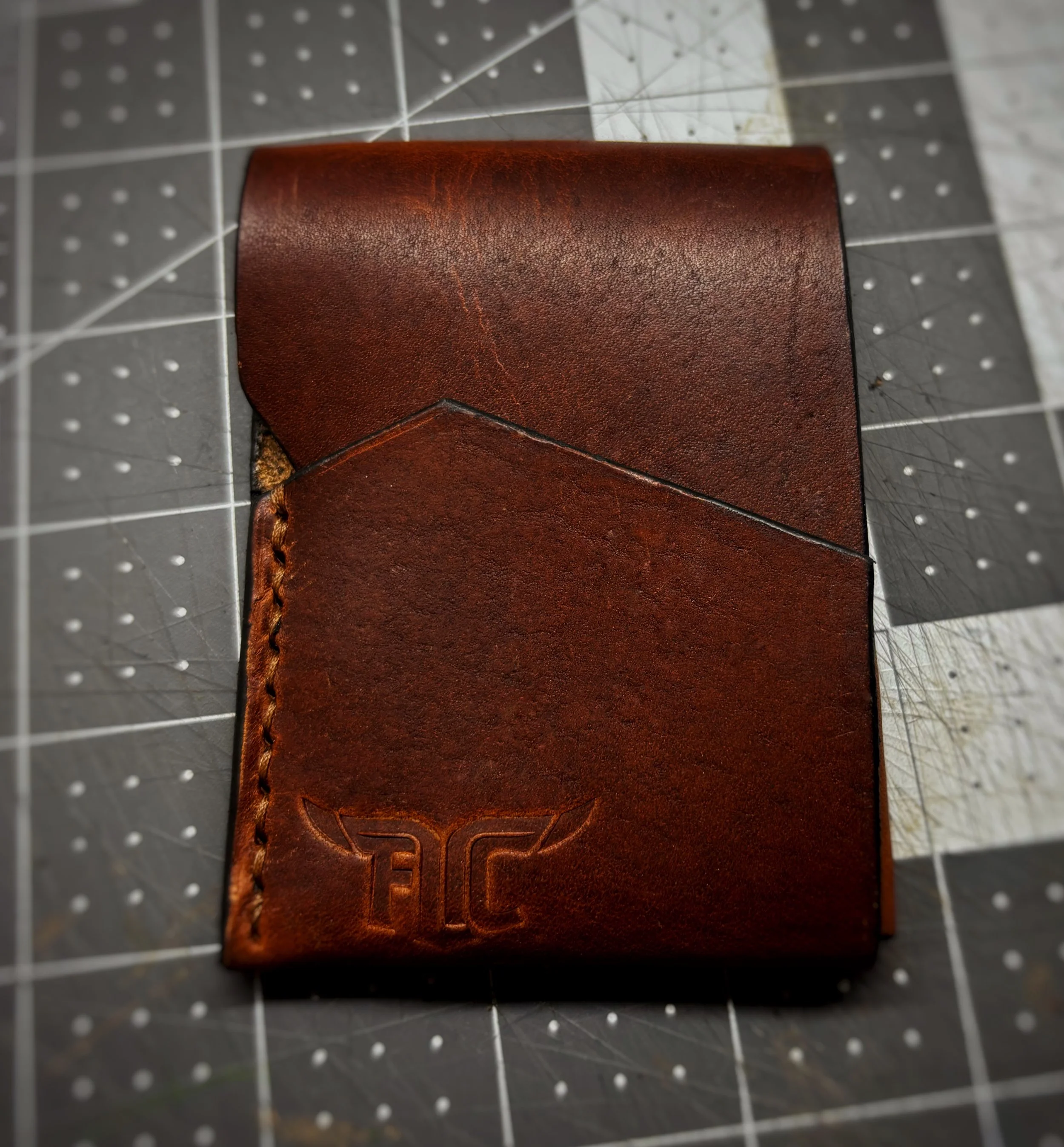 A brown leather wallet with an embossed logo featuring wings and the letters 'FC' on the bottom right corner.