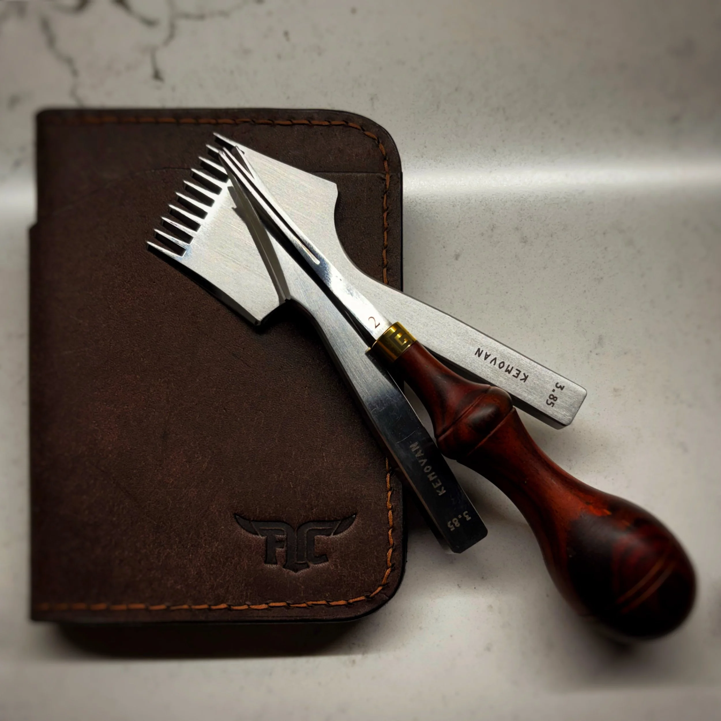 A leather wallet with a metal beard and mustache comb and a straight razor on top of it.