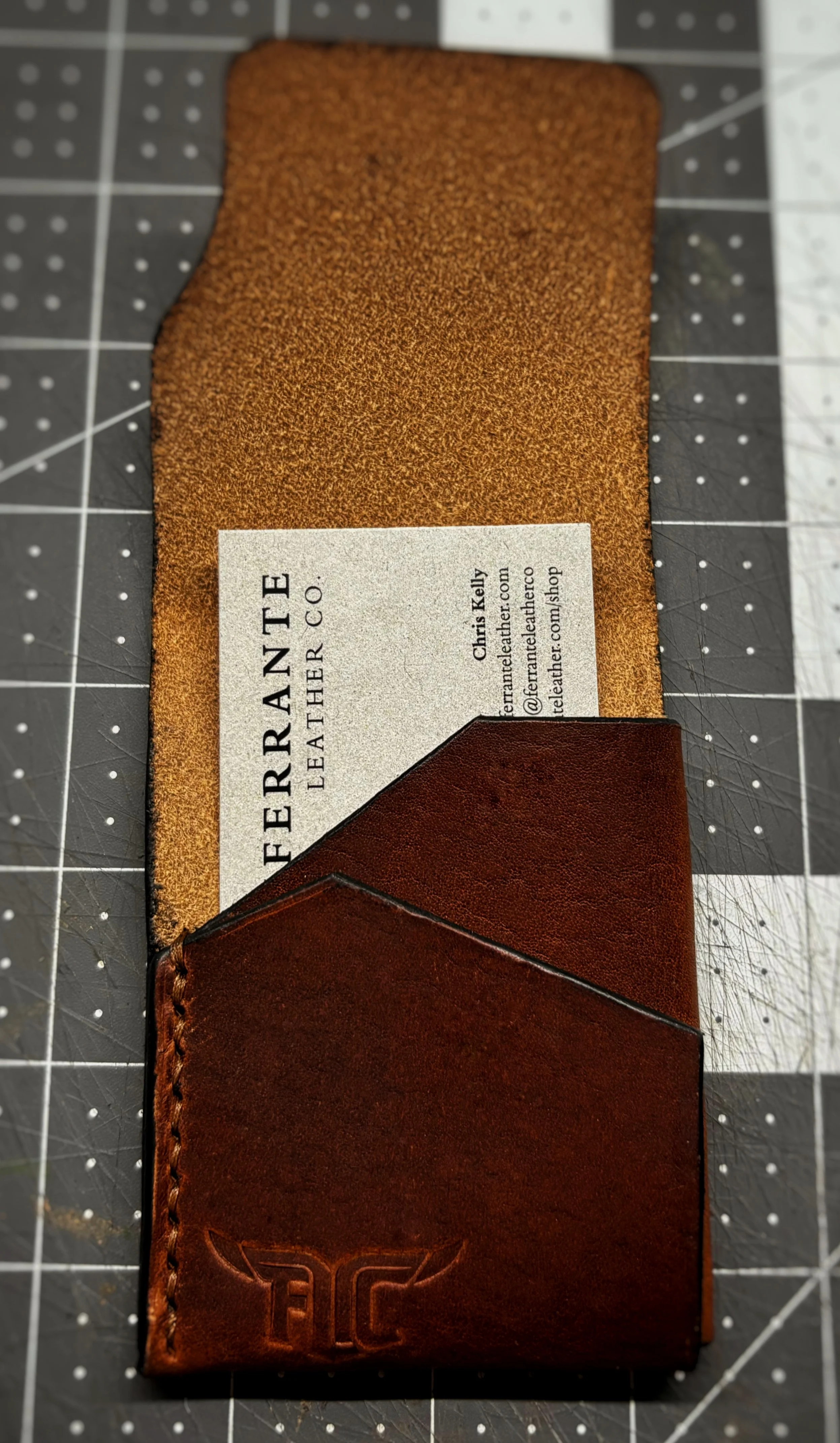 Close-up of a leather wallet with a business card inside, placed on a cutting mat.
