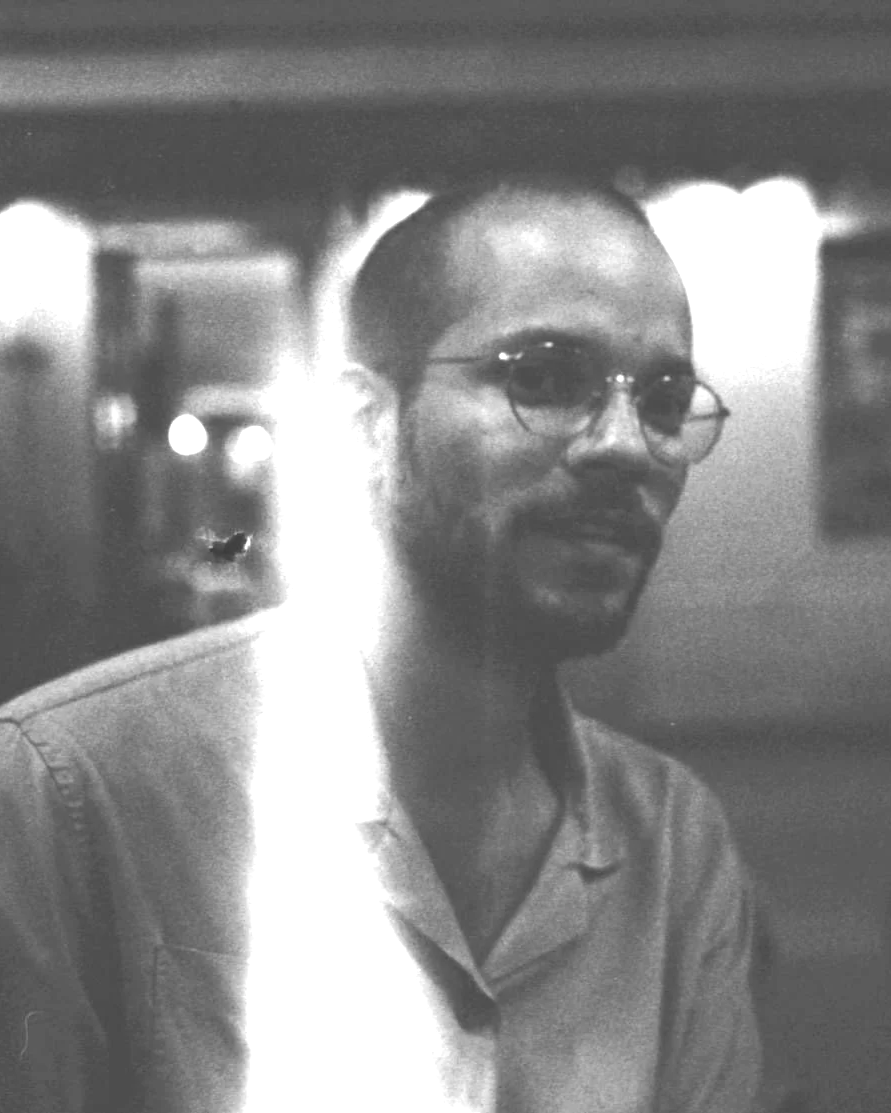 Un homme portant des lunettes et une chemise clair, en train de sourire, dans un cadre intérieur.