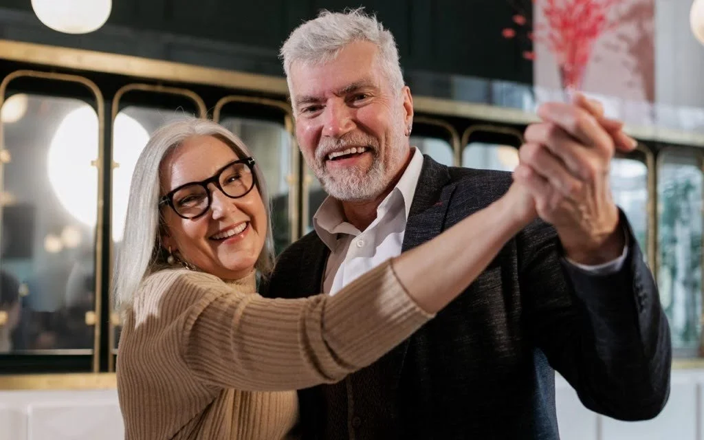 Coppia sorridente che balla tenendosi per mano: imparare a ballare a 50 anni è possibile e divertente, anche in un elegante locale.
