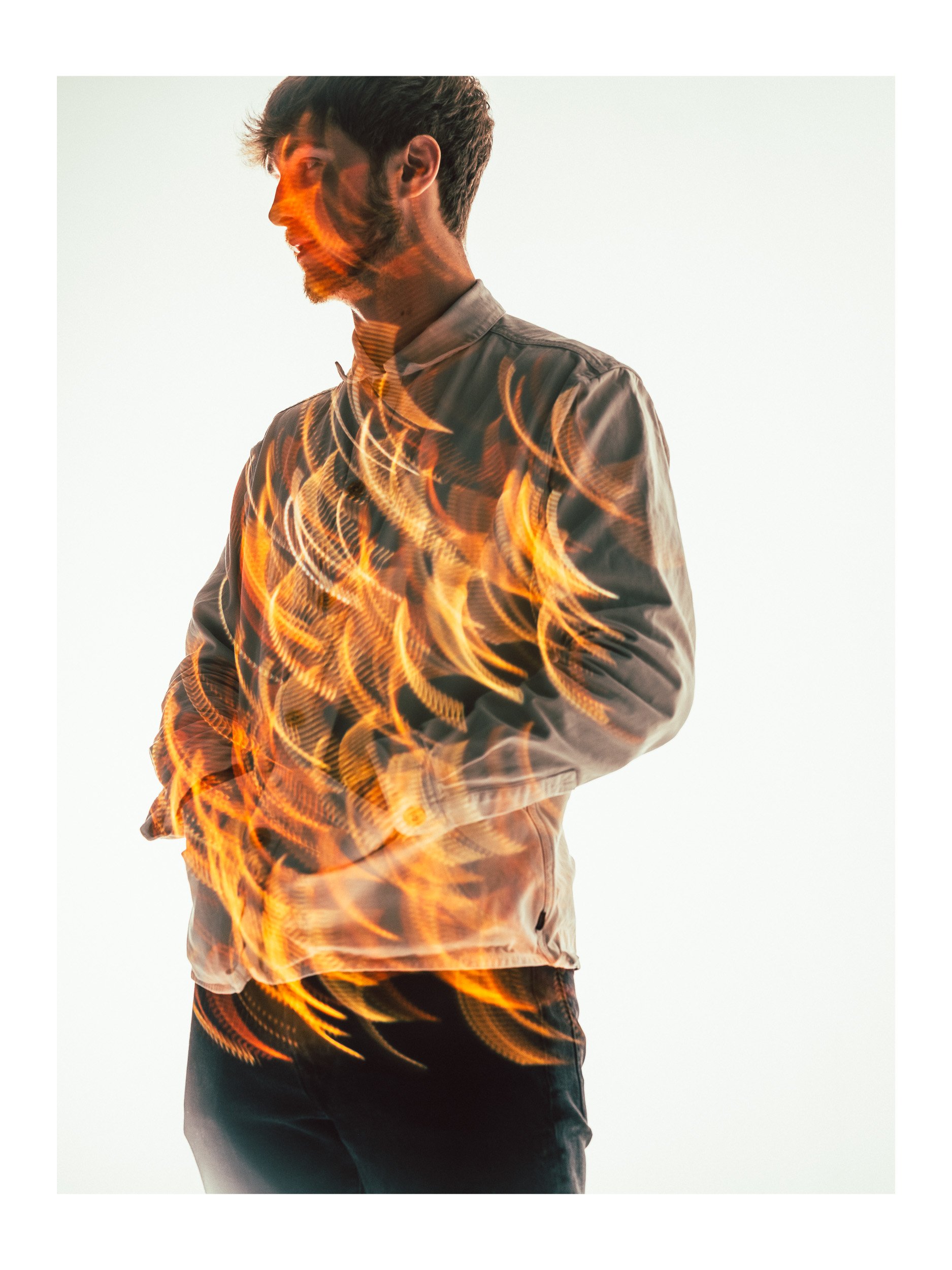 A young man in a gray jacket standing against a plain white background with swirling light trails.