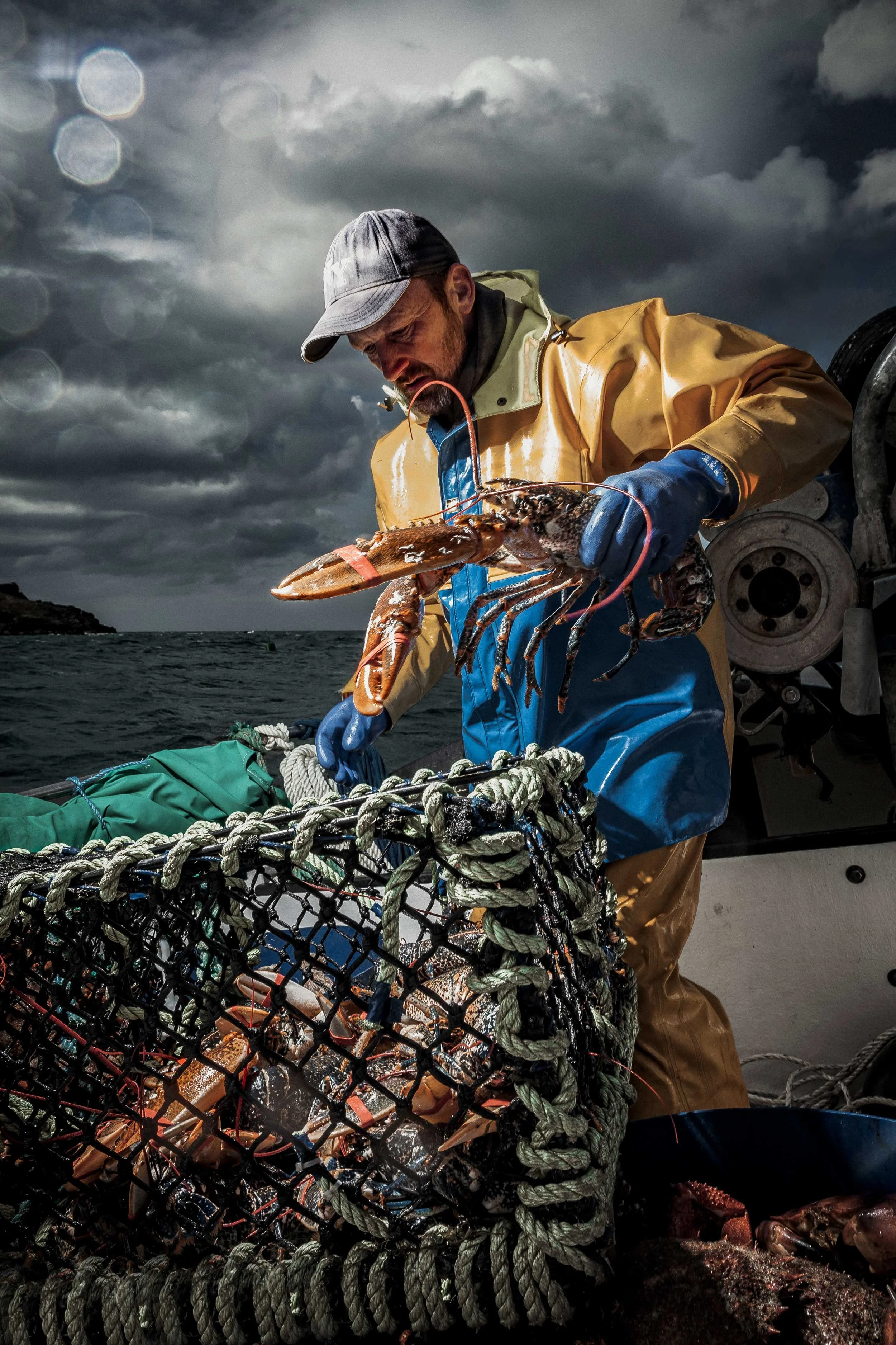 A man in waterproof gear and gloves holding a lobster on a boat during a stormy day with dark clouds and choppy water in the background.