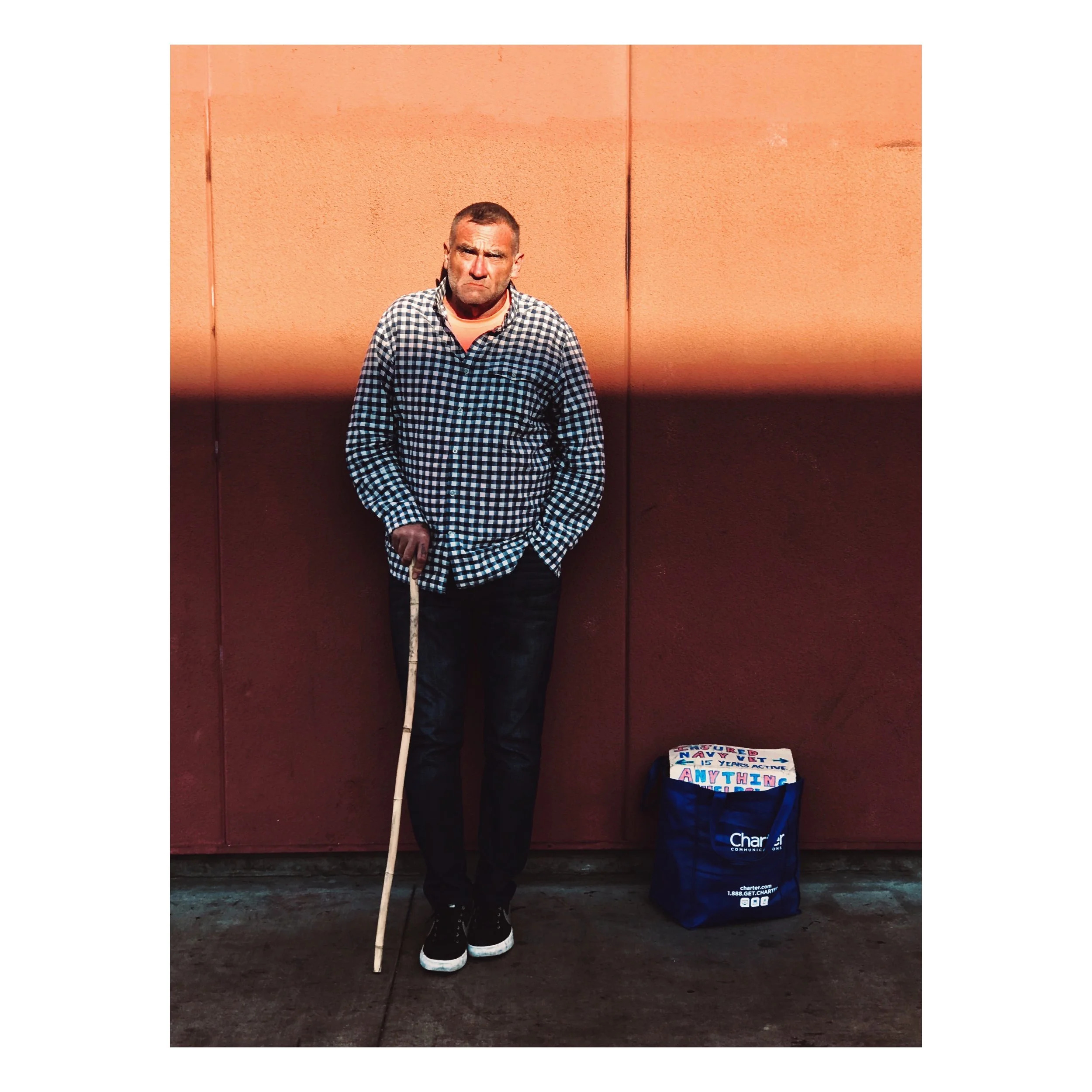 A man standing outdoors in front of a closed light-colored metal garage door, wearing a gray blazer, white shirt, black pants, and tan shoes.