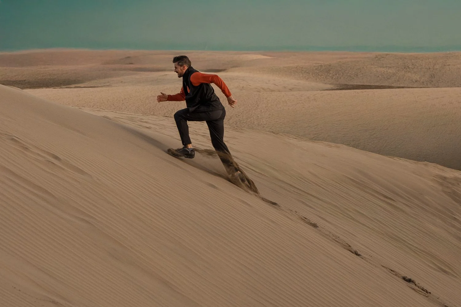 A man climbing a sand dune in a desert.