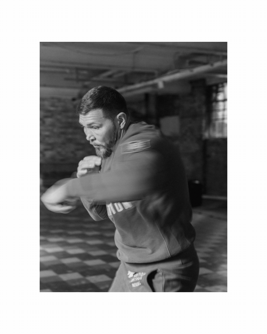 A man with a beard practicing martial arts in a gym, wearing sports clothing and executing a punch.