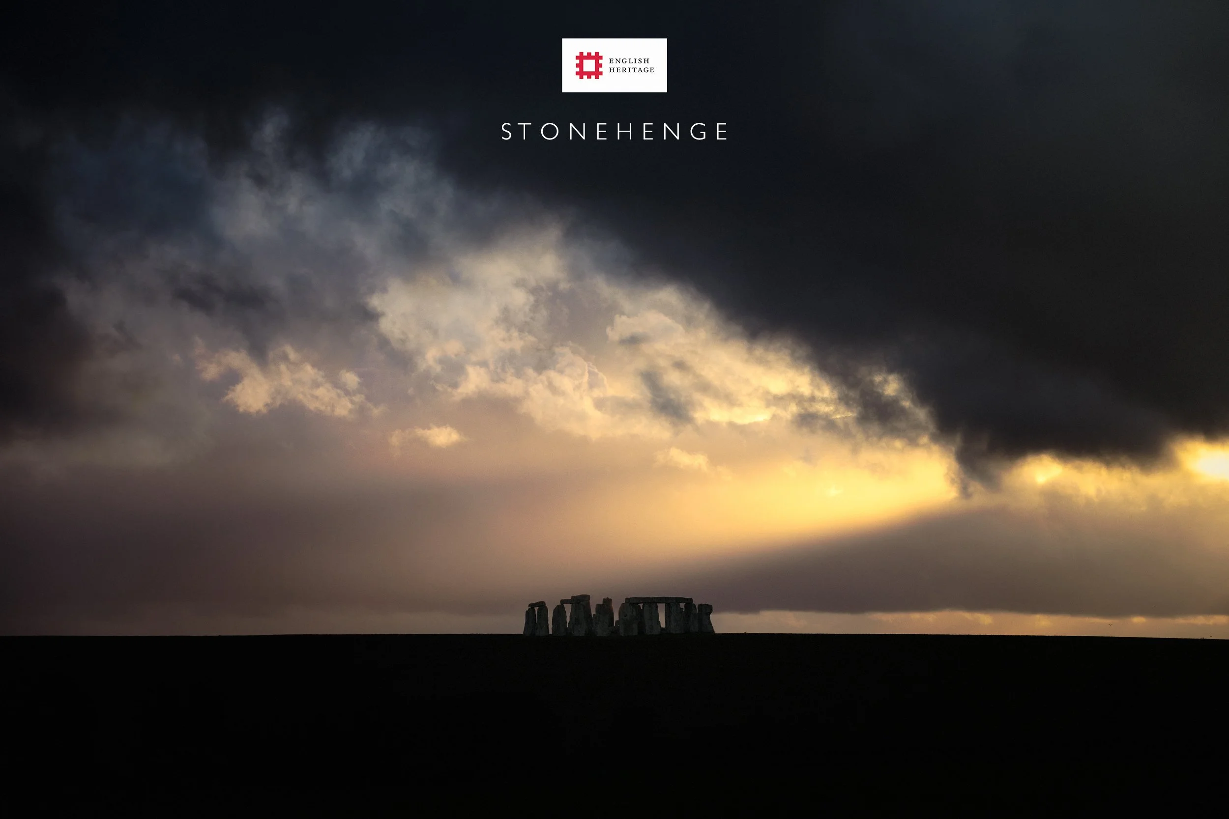 Sunset over Stonehenge with dark clouds in the sky and the ancient stone circle silhouetted against the horizon.