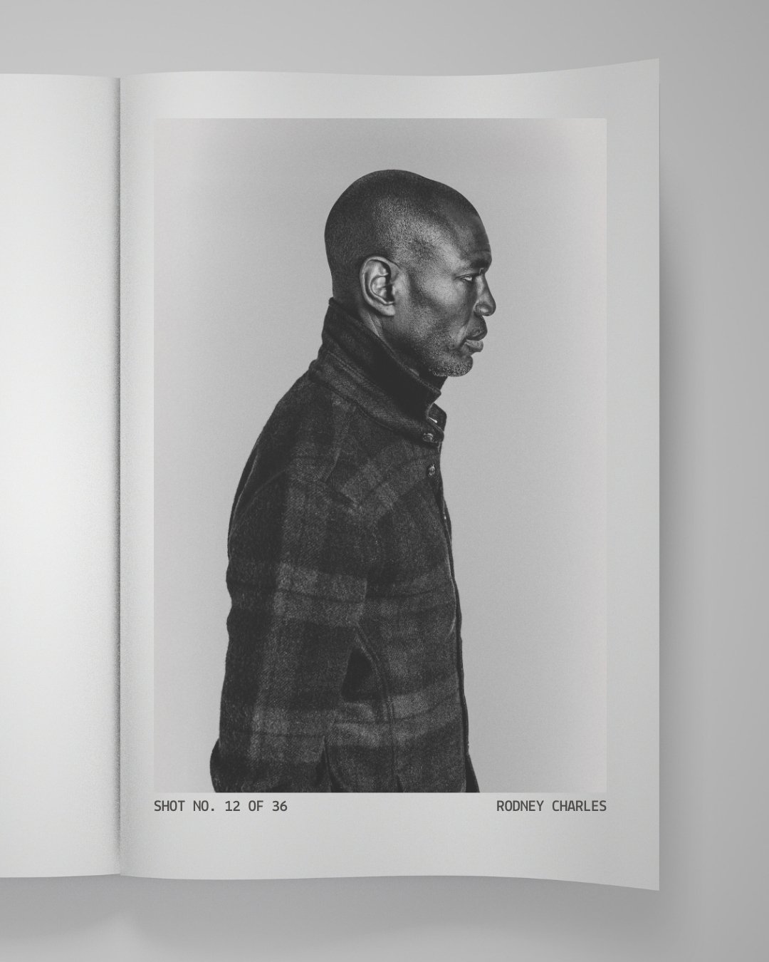 Black and white photo of Rodney Charles in profile view, wearing a plaid jacket.