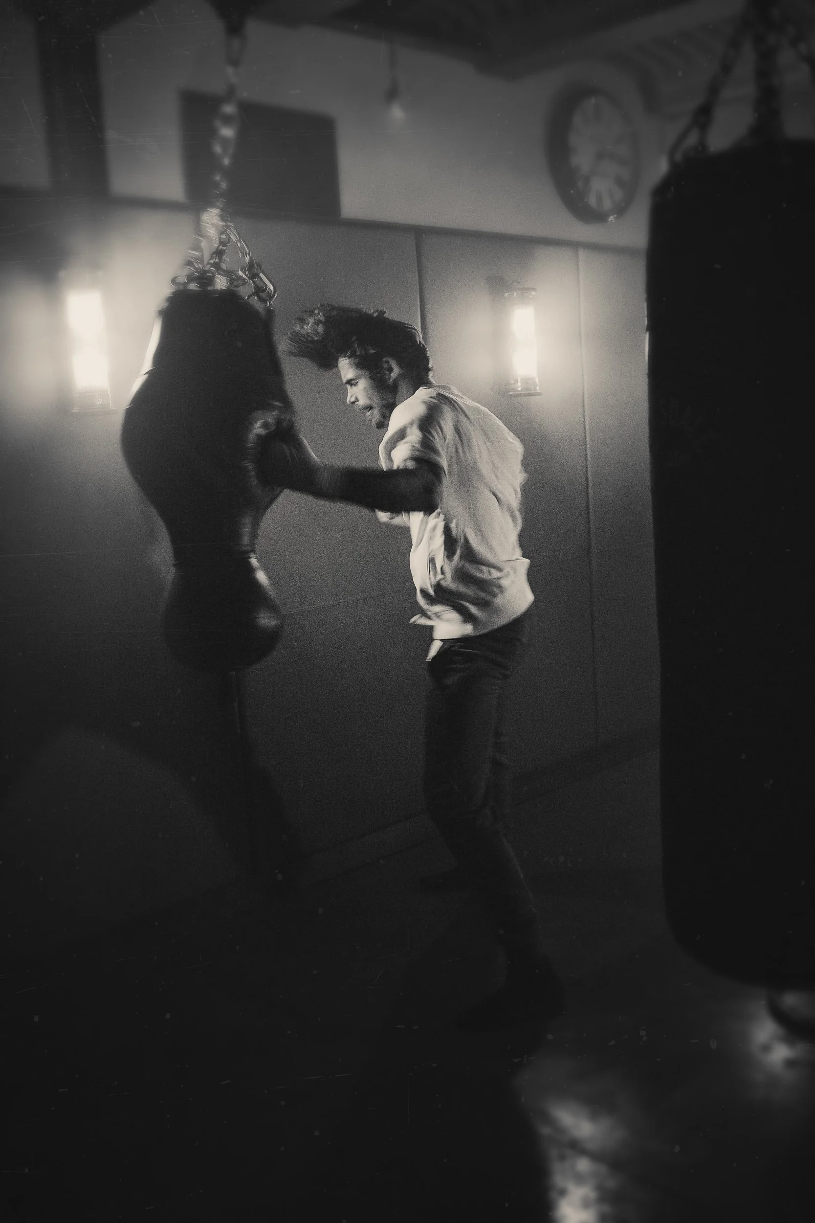 A young man with long hair boxing with a punching bag in a gym, black and white image.