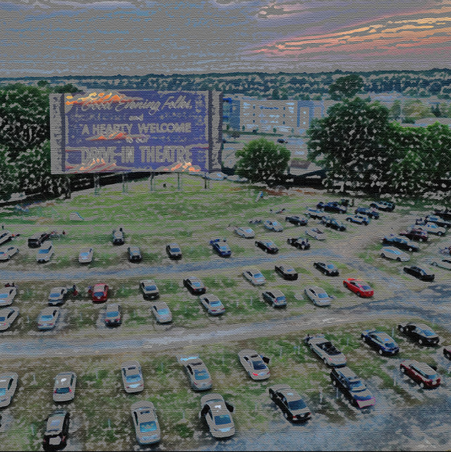 A parking lot filled with cars, with a grassy area and trees behind it. In the background, there is a large billboard and several buildings under a cloudy sky.