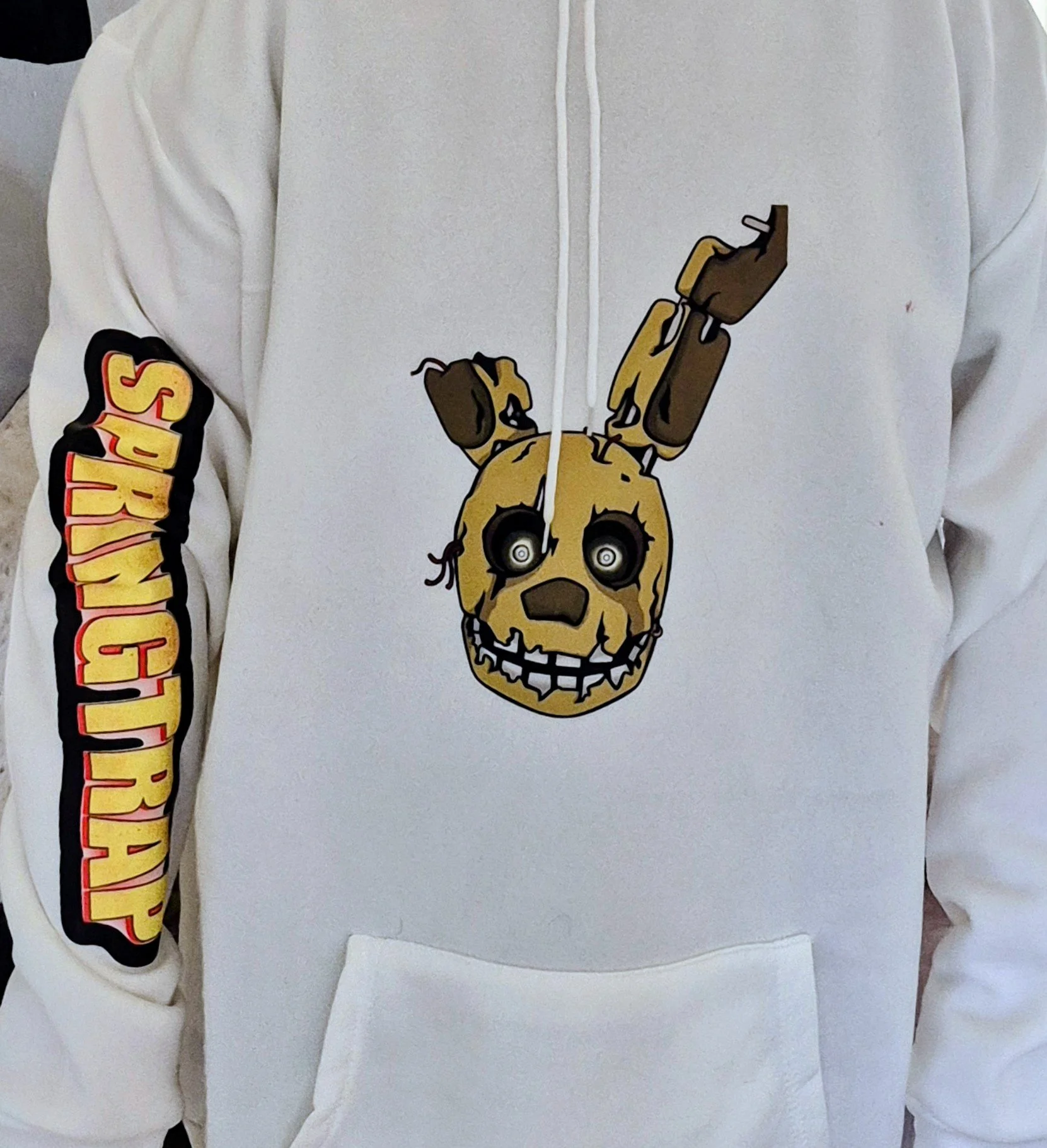 Person wearing a white hoodie with a graphic of five nights at freddy's springtrap on then word springtrap going down the sleeve.