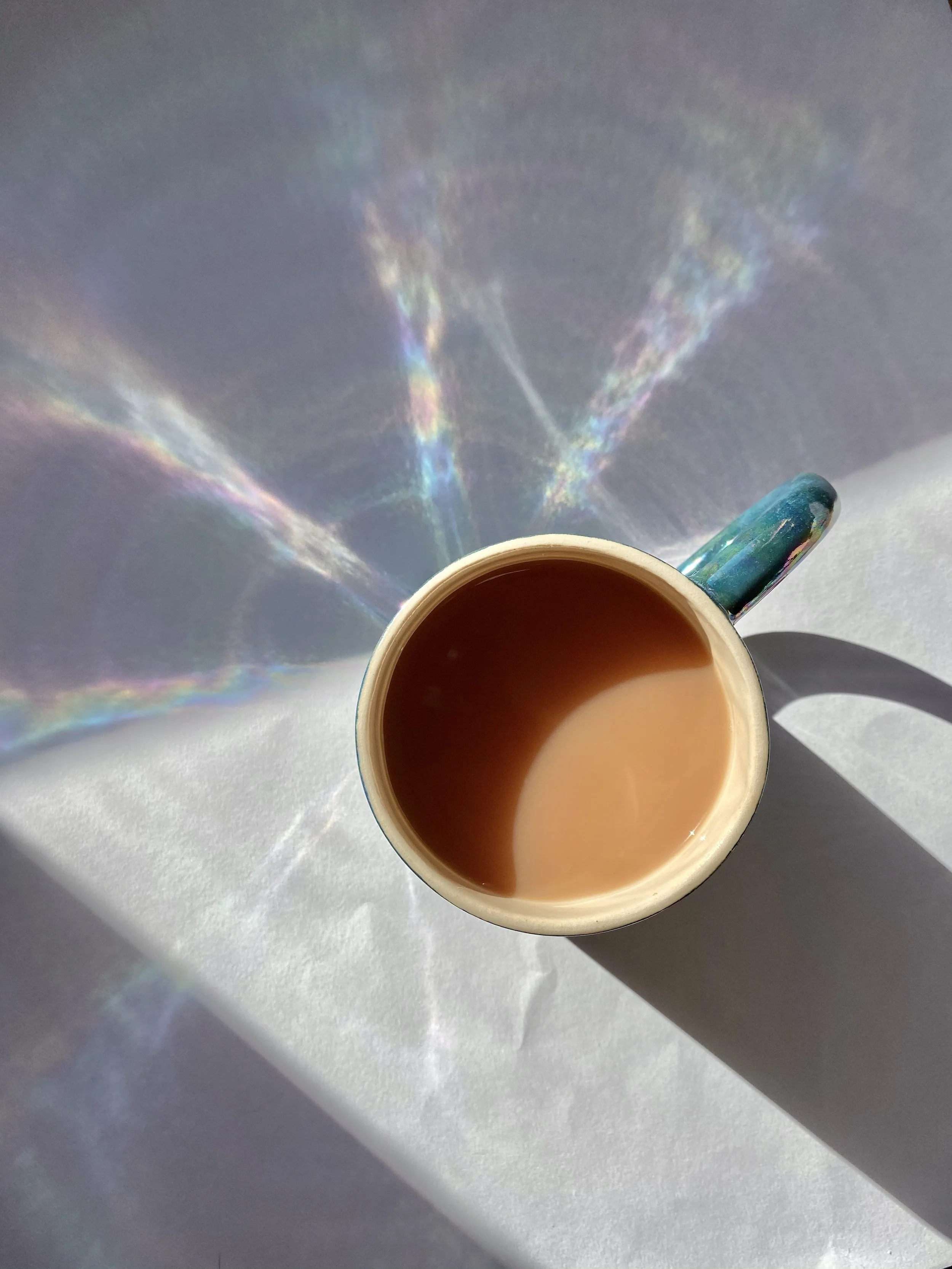 A cup of tea with an iridescent rainbow reflection cast from the lustre glaze onto the surface of a table.