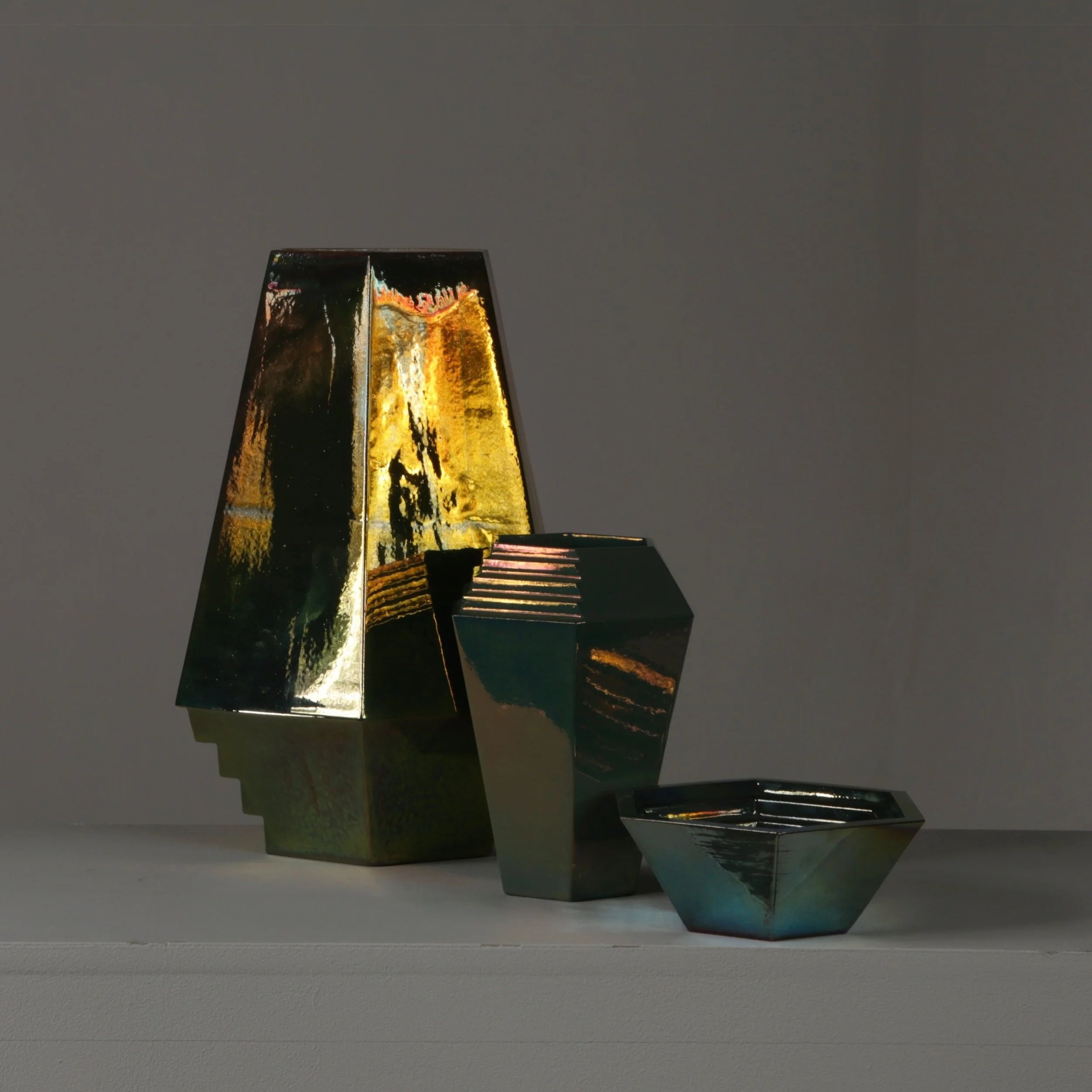 A collection of three iridescent vessels, made by Alison Thyra Ceramics, of varying shapes and sizes arranged on a white surface against a plain background.