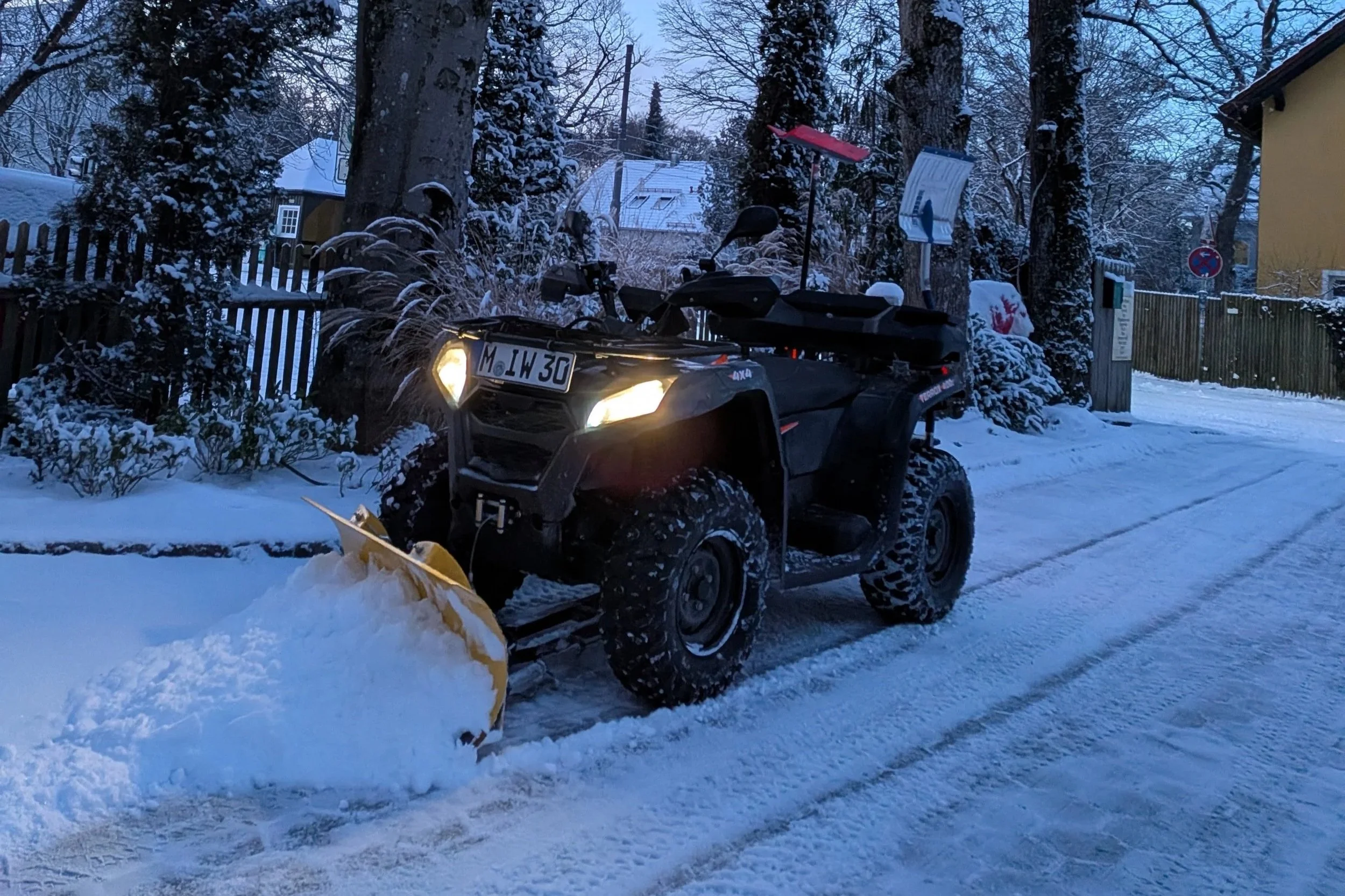 Ein Quad mit Schneeschaufel im verschneiten Außenbereich bei Dämmerung.