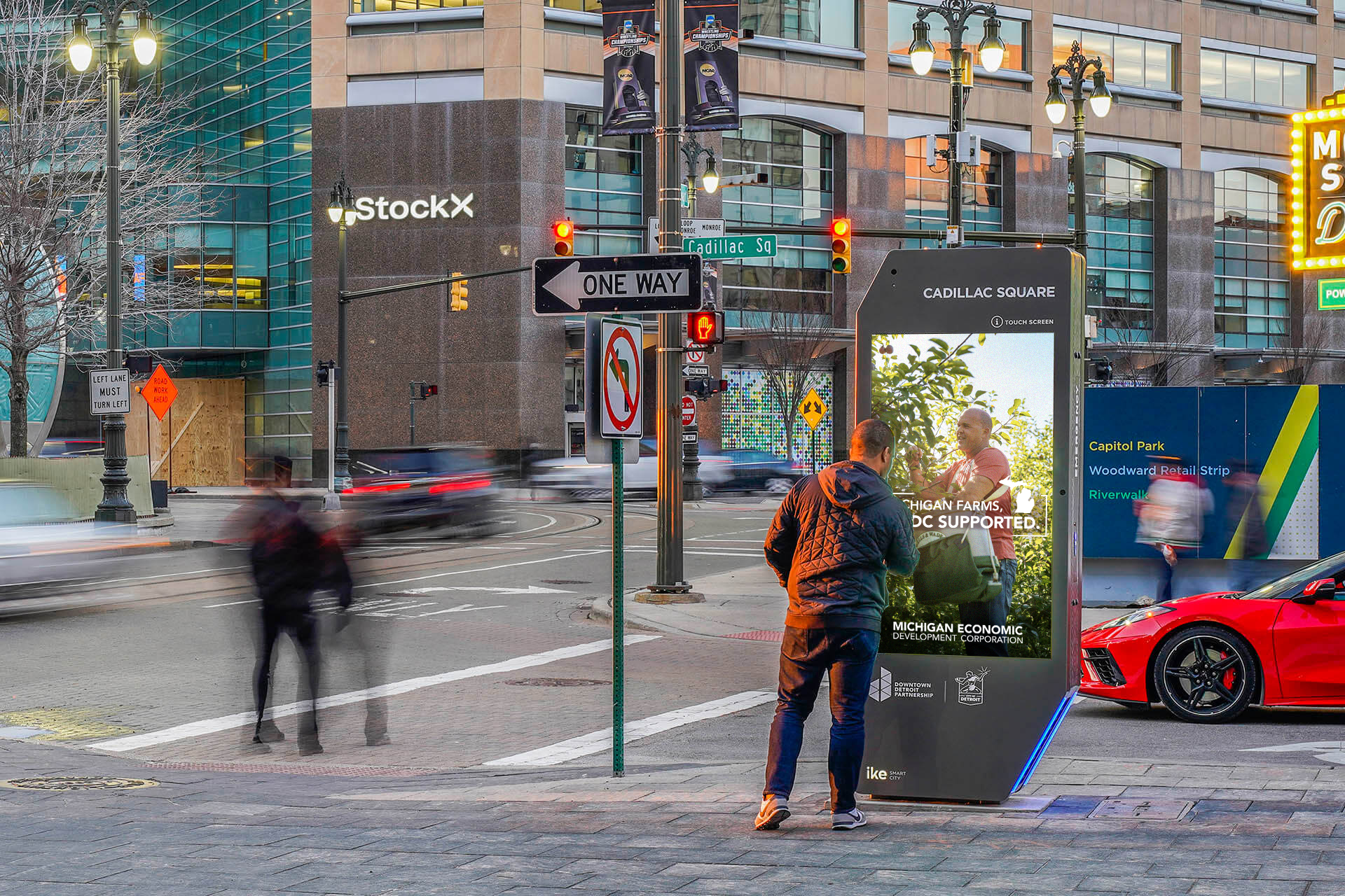 Vertical digital street kiosk mockup displaying a "Michigan Made, MEDC Supported." advertisement with a farmer picking apples, located on a sunny city sidewalk. Created by Detroit based Art Director and Designer Justin Scott.