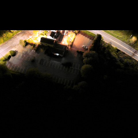 Aerial night-time video captured by a drone showing a lit commercial building and car park, demonstrating low-light surveillance and facility monitoring capabilities.