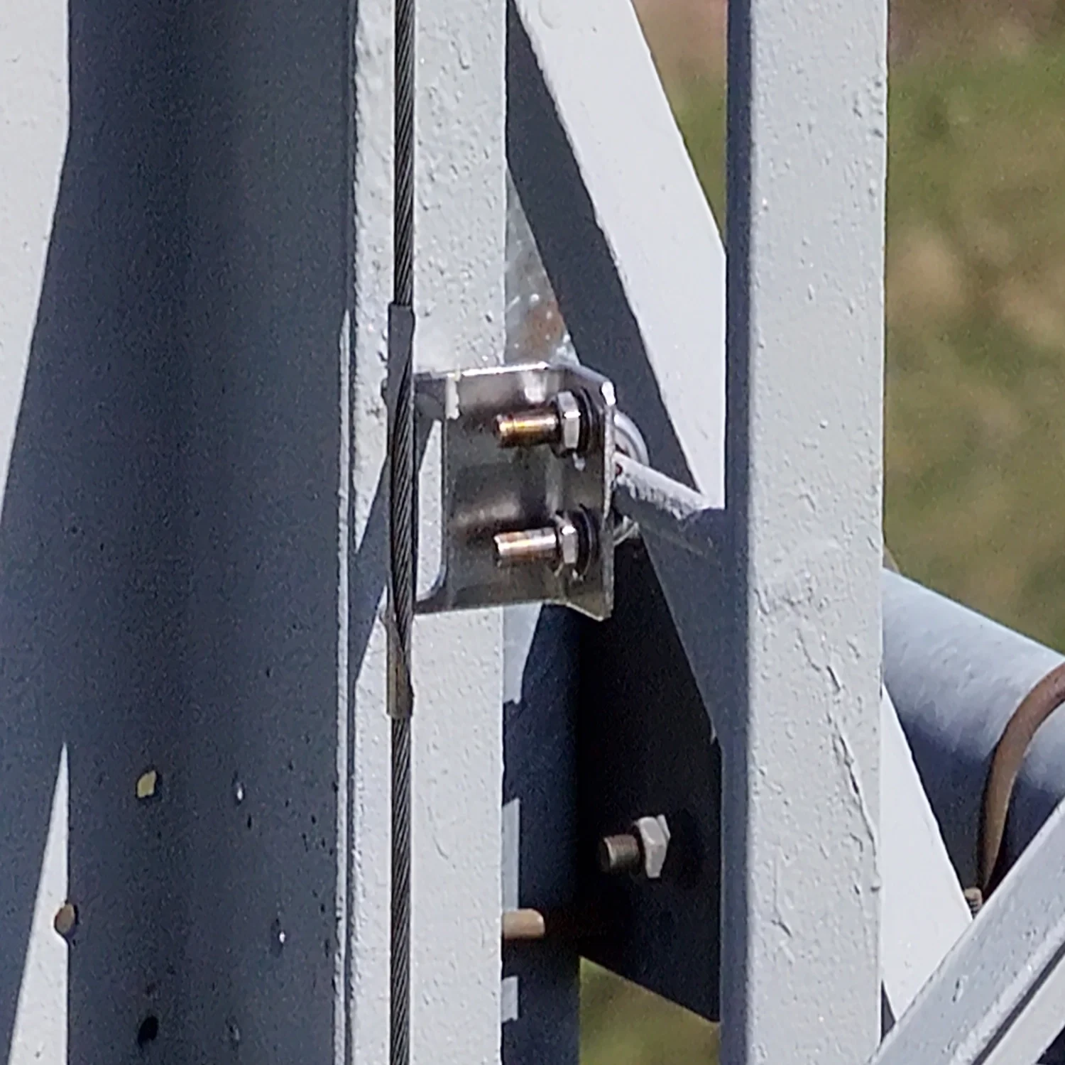 Extreme close-up drone inspection photo of steel mounting brackets, nuts, and tension cables on a telecommunications mast to check for loosening or structural wear.